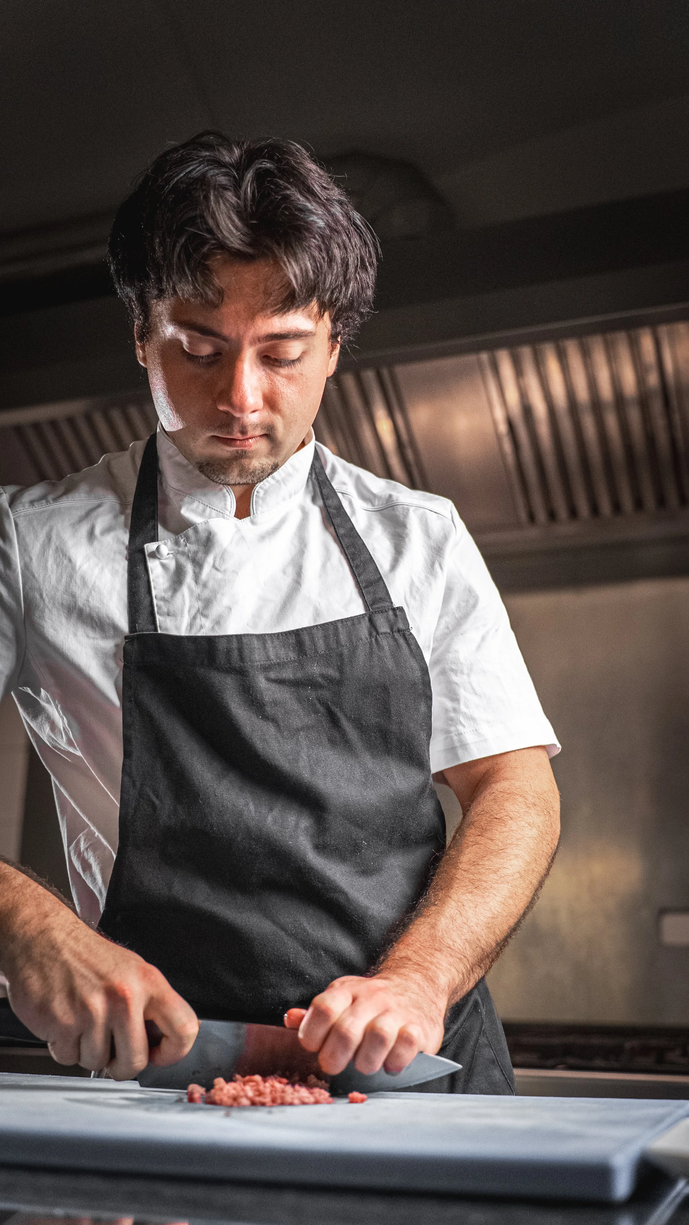 Uno chef che sta tritano la carne su un tagliere in cucina.