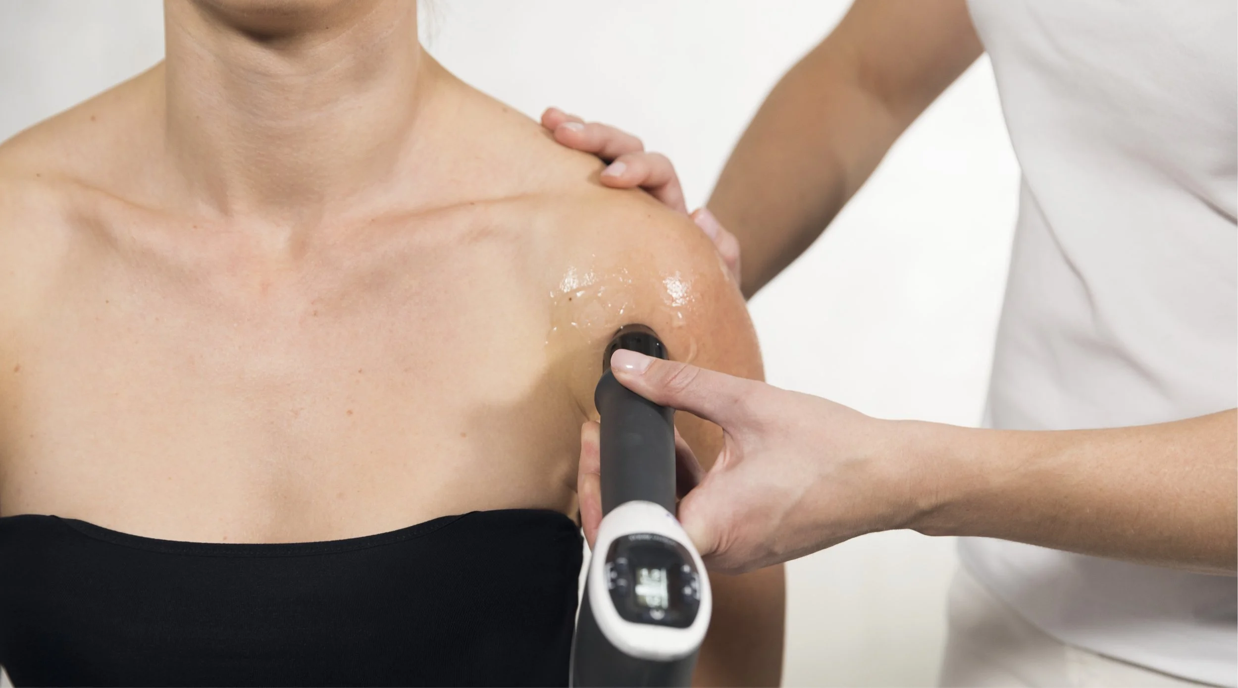 A person undergoing a breast examination using an ultrasound device in a medical setting with a healthcare professional.