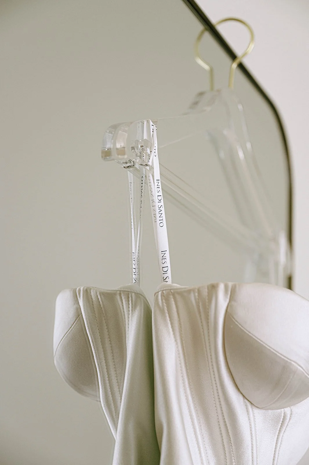 Close-up of a white dress hanging on a clear plastic hanger from a black metal rod, with a neutral-colored background.