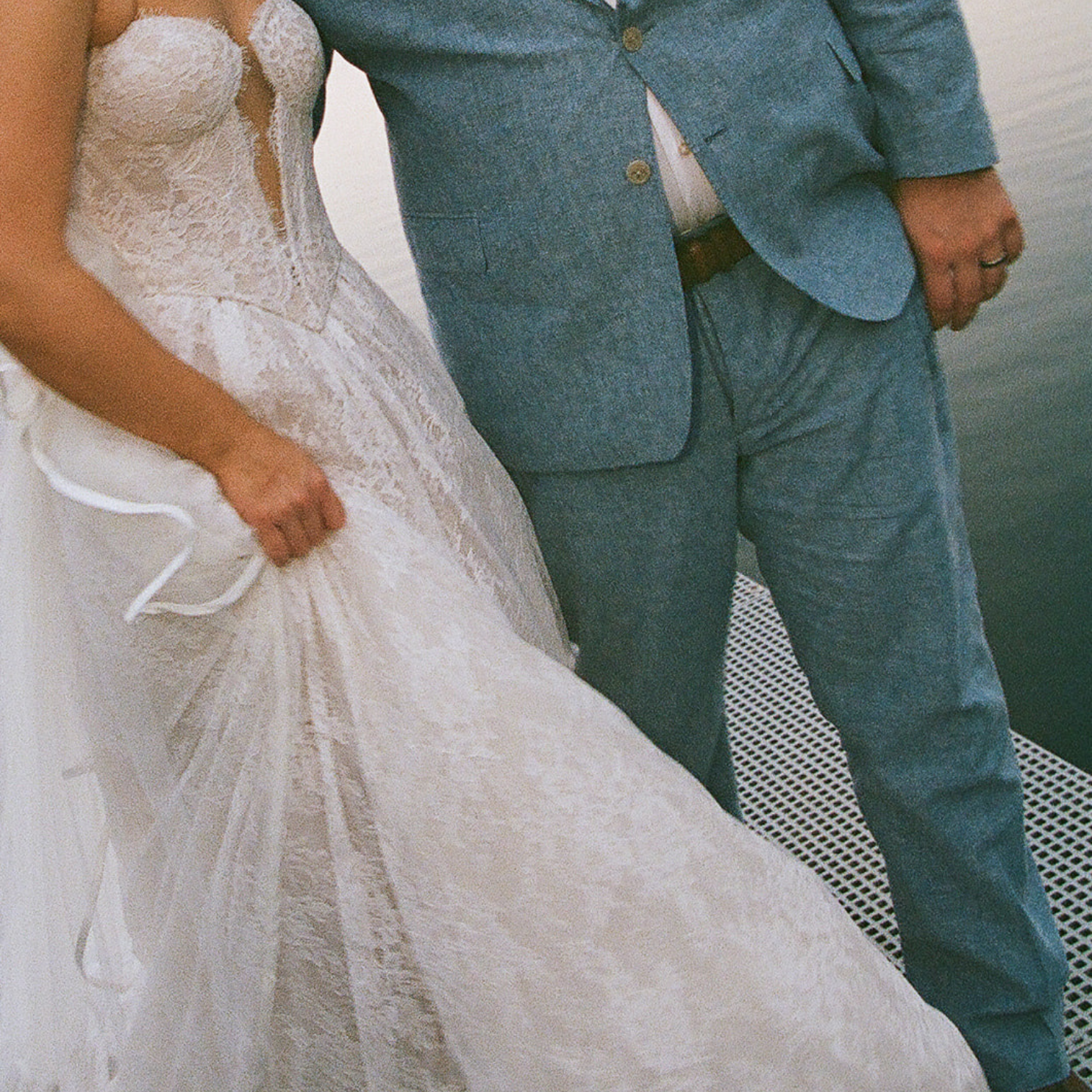 A bride in a lace wedding dress standing next to a man in a light blue suit on a boat.