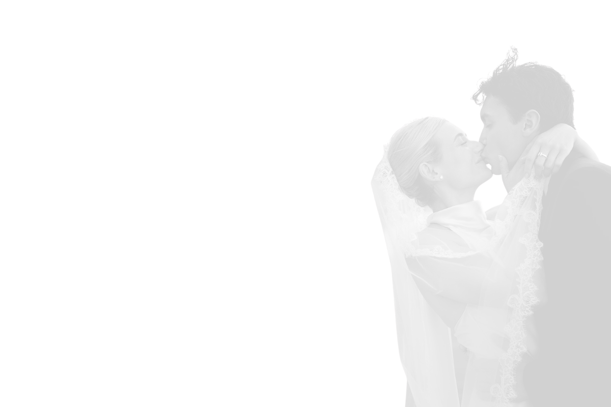 Black and white photo of a bride and groom sharing a kiss. The bride has a lace veil and is wearing a wedding dress, while the groom is in a suit.