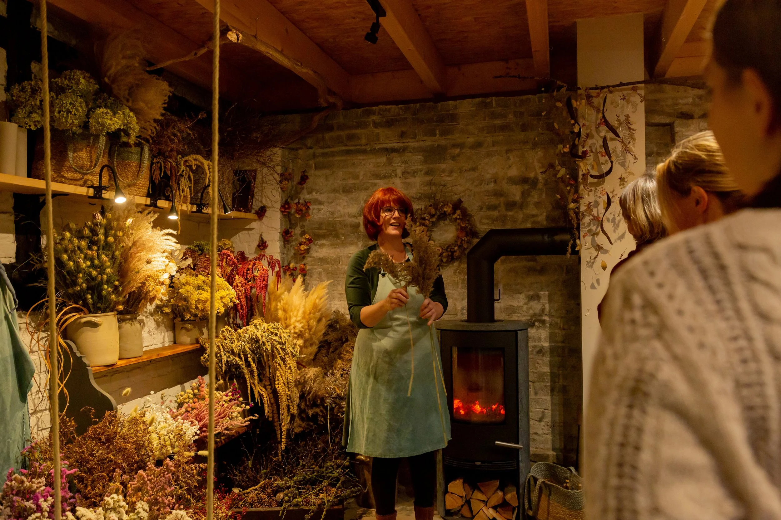 Workshop mit Trockenblumen bei Blumenworkshop. Marie Cramer erklärt den Workshopteilnehmern die Trockenblumen. Das Atelier wird mit einem Holzofen beheizt.