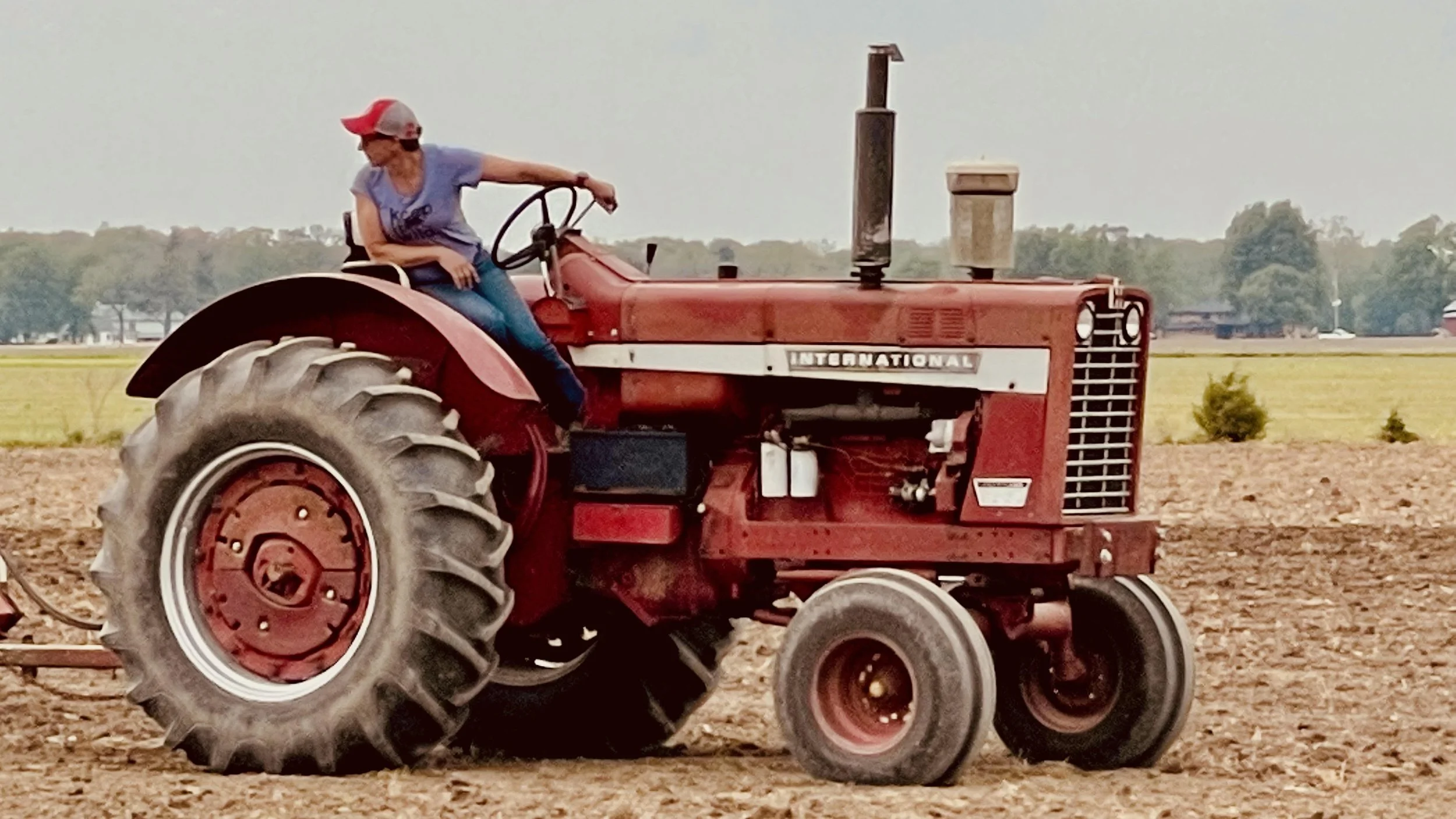 Sarah riding a red tractor across a farm field.