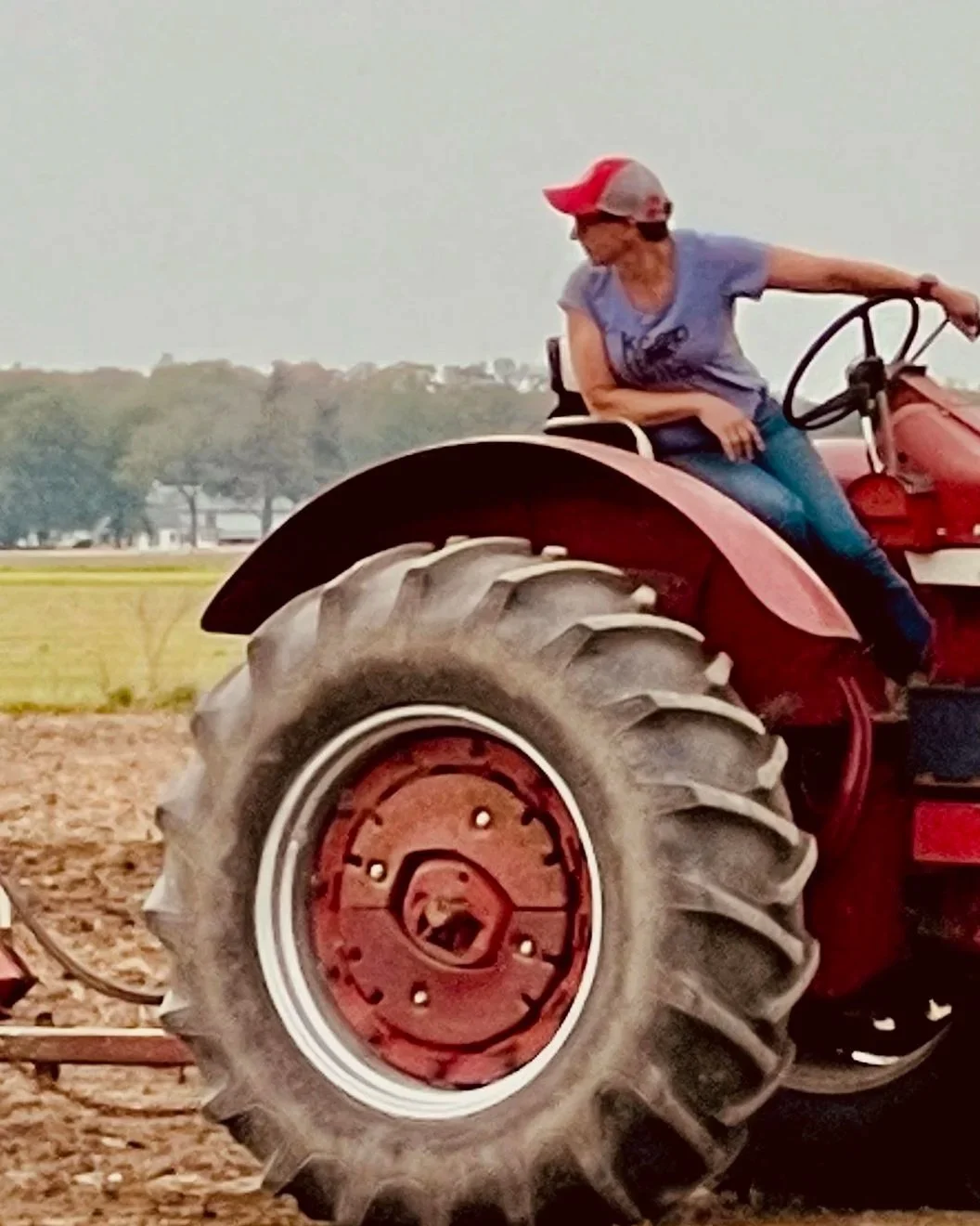Sarah riding a IH 856 tractor in a field, wearing a cap and sunglasses.