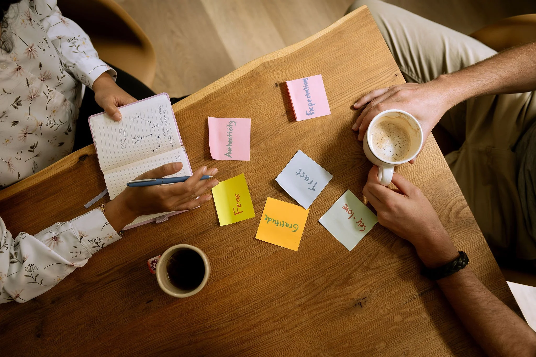 A coaching session with colorful sticky notes labeled “Authenticity,” “Expectations,” “Trust,” “Gratitude,” and “Self-Love,” alongside two cups of coffee on a wooden table.