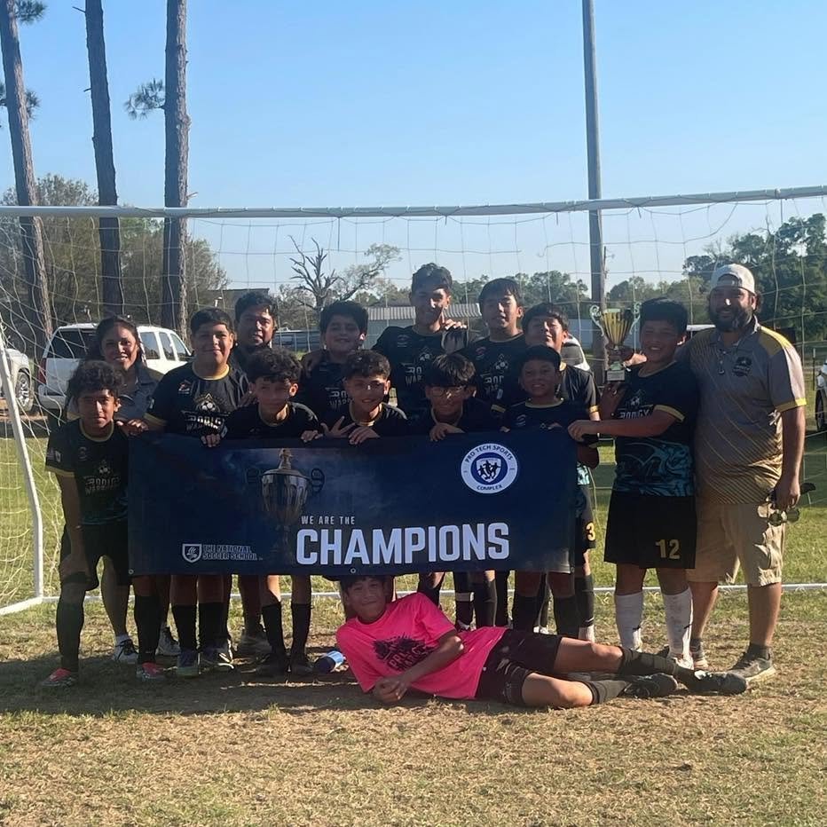 A youth soccer team with their coach holding a banner that says 'We are the Champions' after winning a tournament, with some players holding a trophy, on a soccer field.