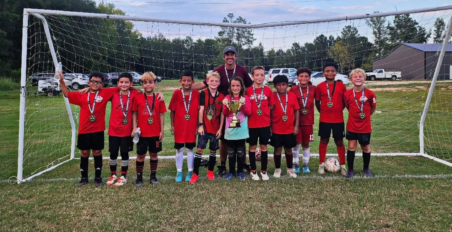 Youth soccer team with medals and a trophy posing with coach on soccer field