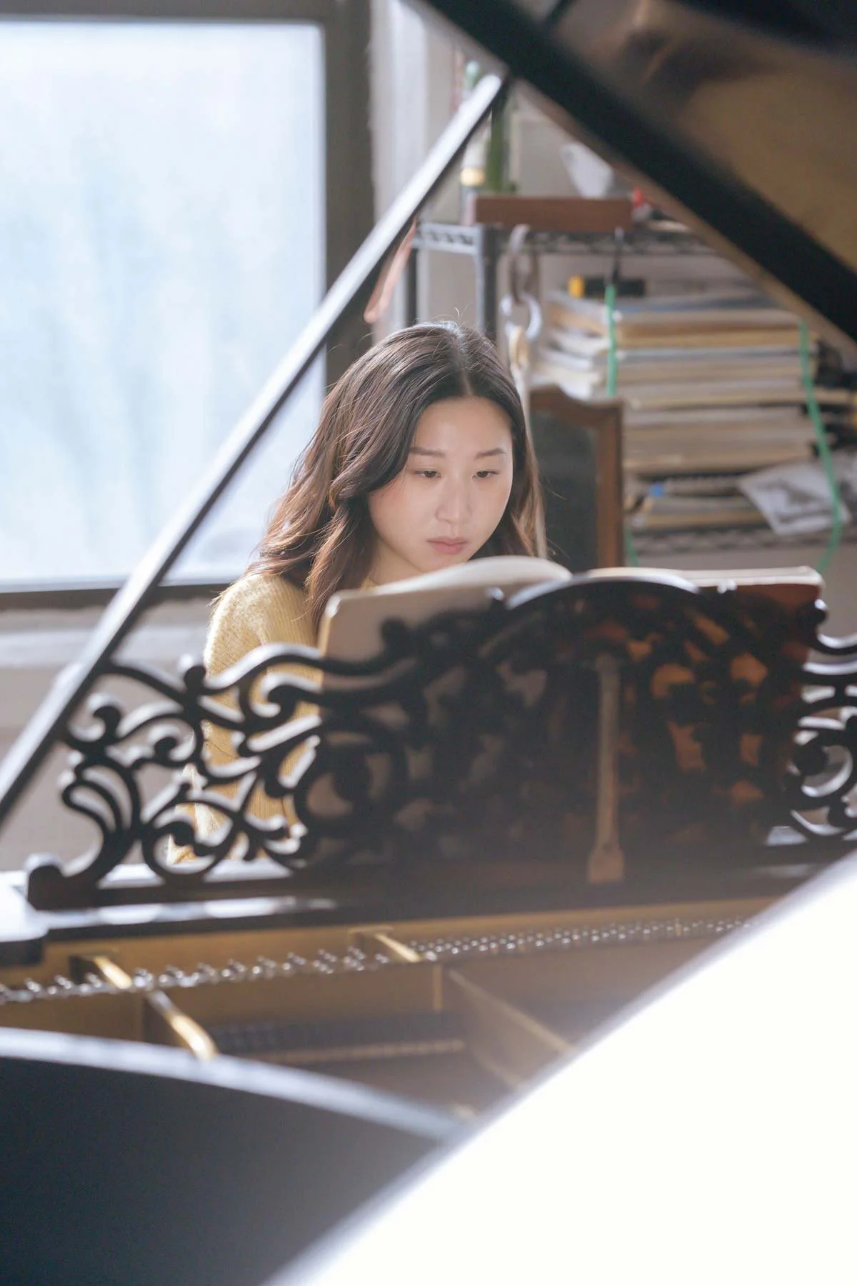 Front view over an ornate black music stand of a woman reading sheet music at a piano