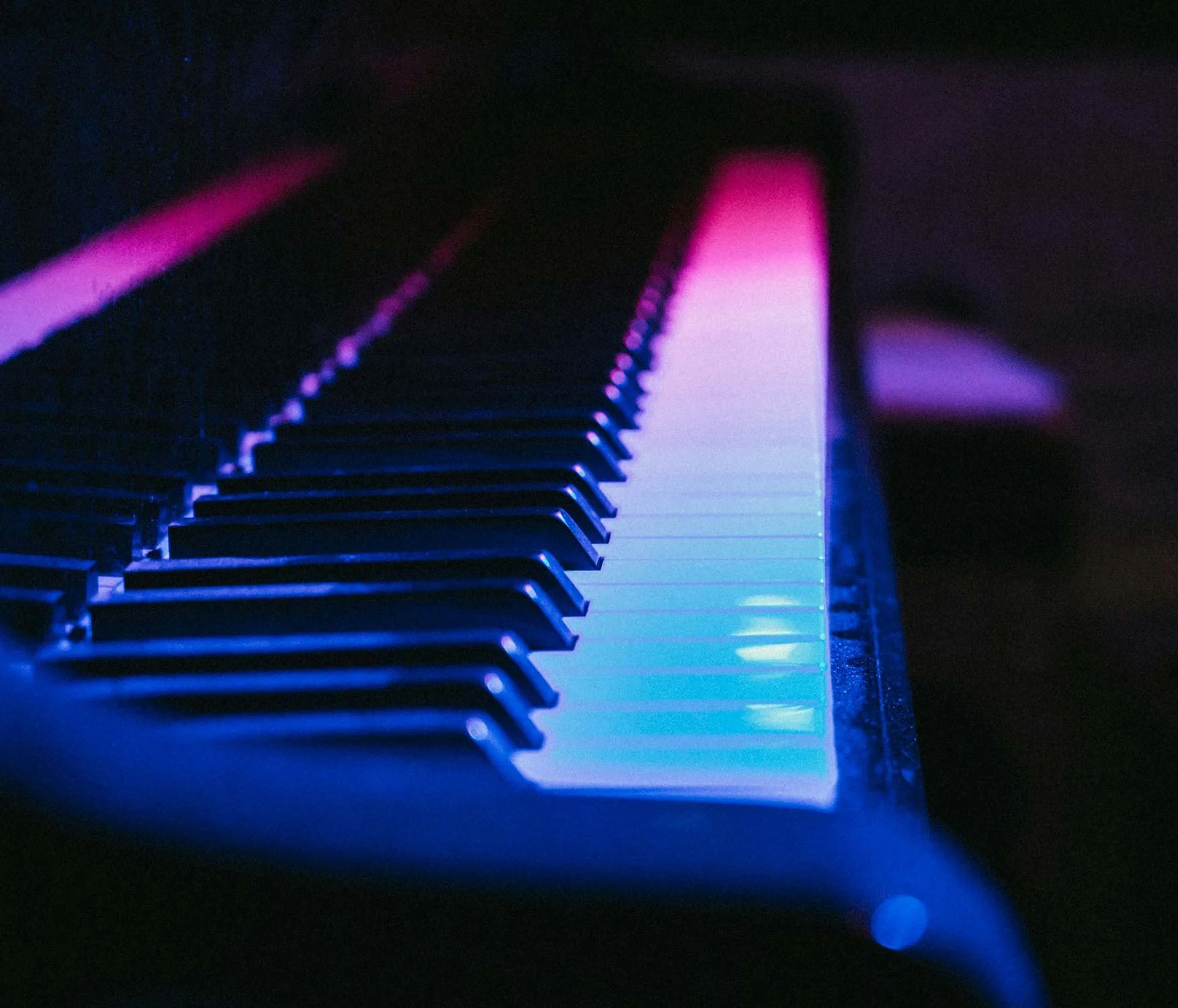A side view of a piano keyboard, lit with pink and blue lights.