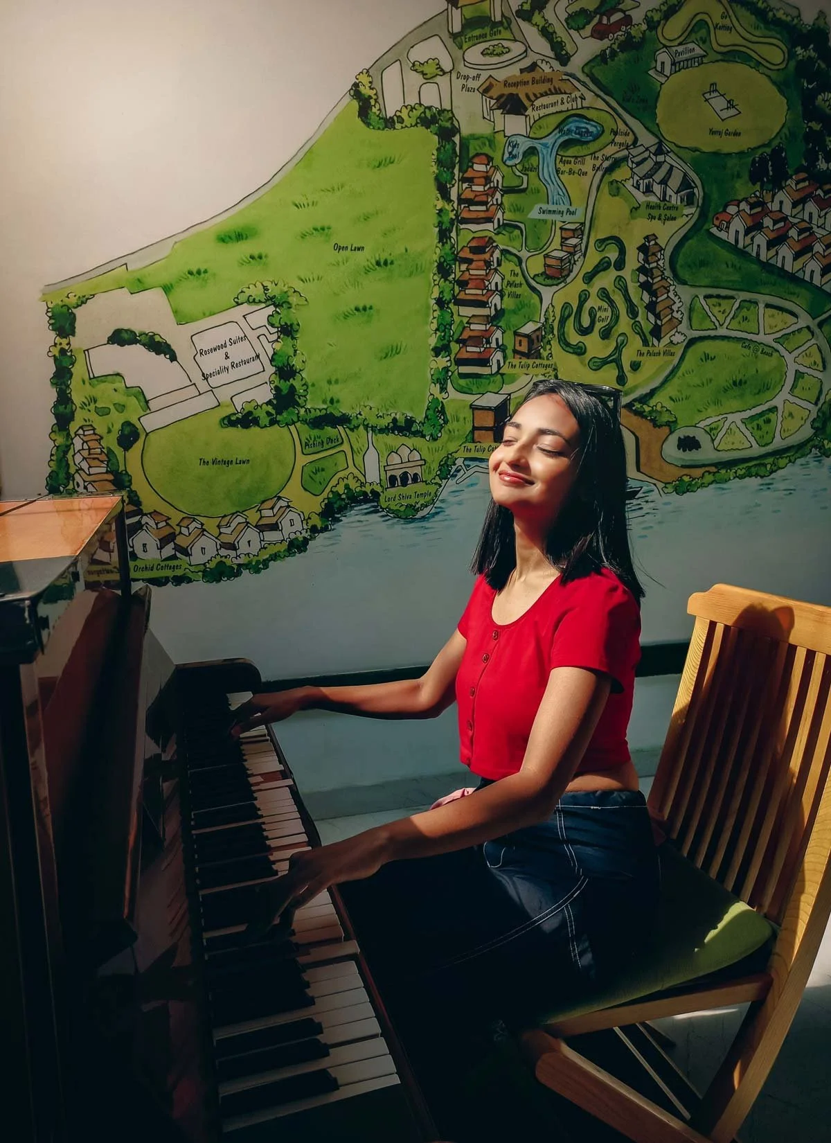 Sideview of a South Asian teen girl with eyes closed playing an acoustic piano with some broken keys