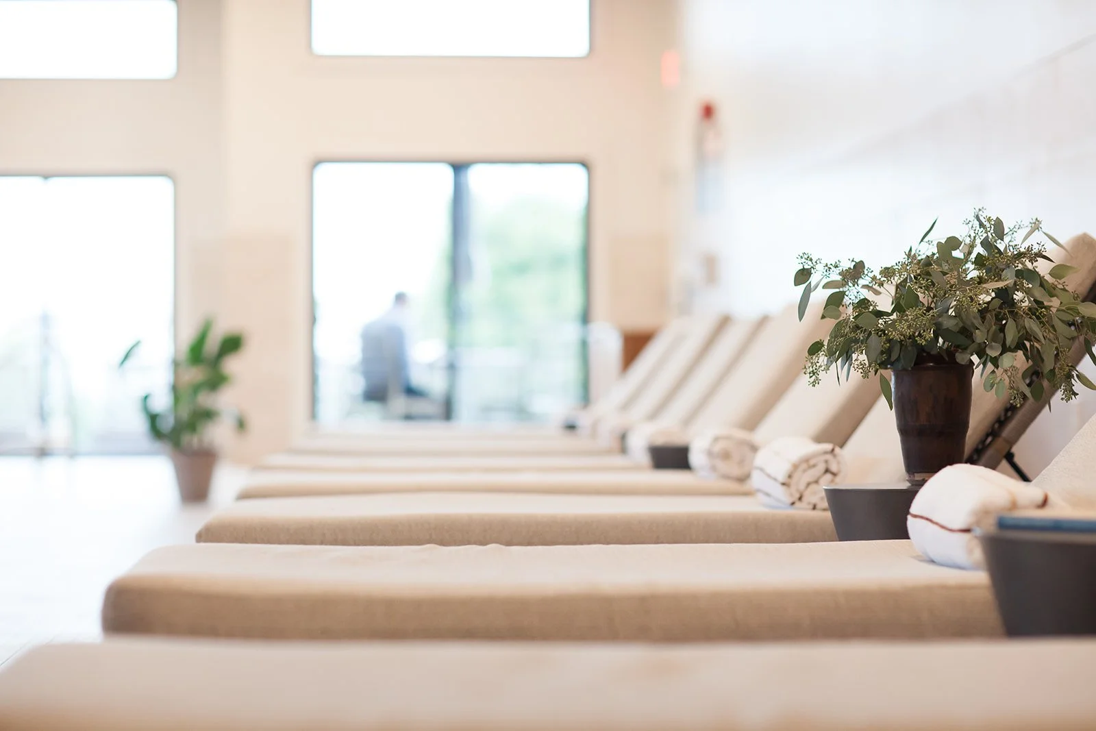 Spa lounge chairs with rolled towels and plants in a bright, modern wellness center.