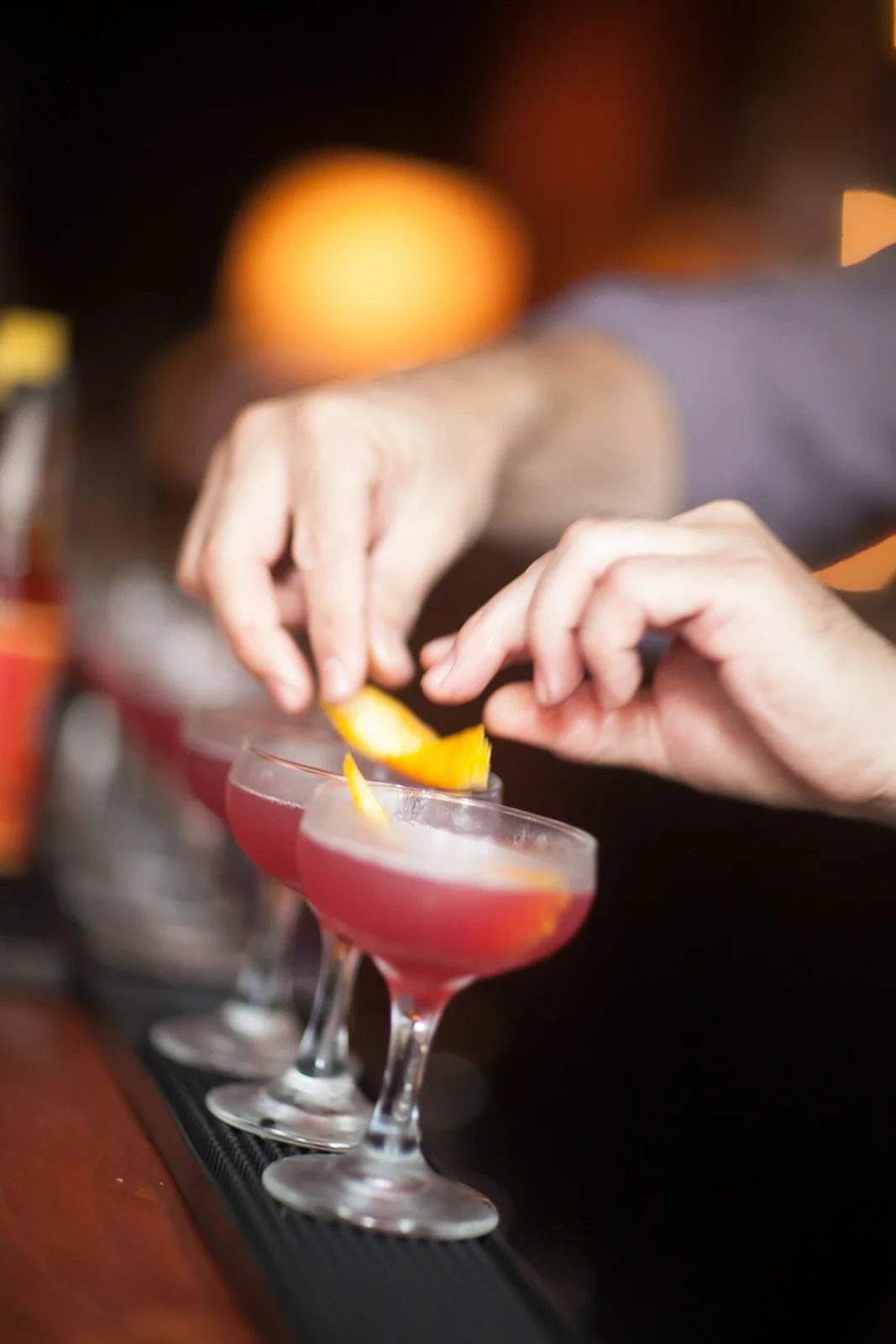 Bartender garnishing cocktails with orange peel at a bar.