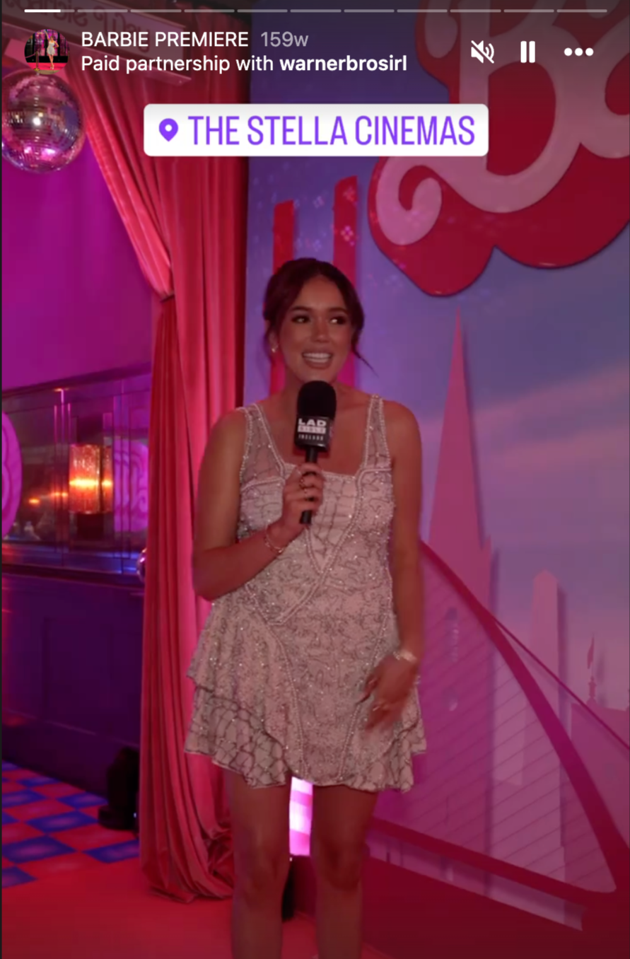 Woman in a sparkly dress holding a microphone at The Stella Cinemas, with pink curtains and a pink and purple backdrop.