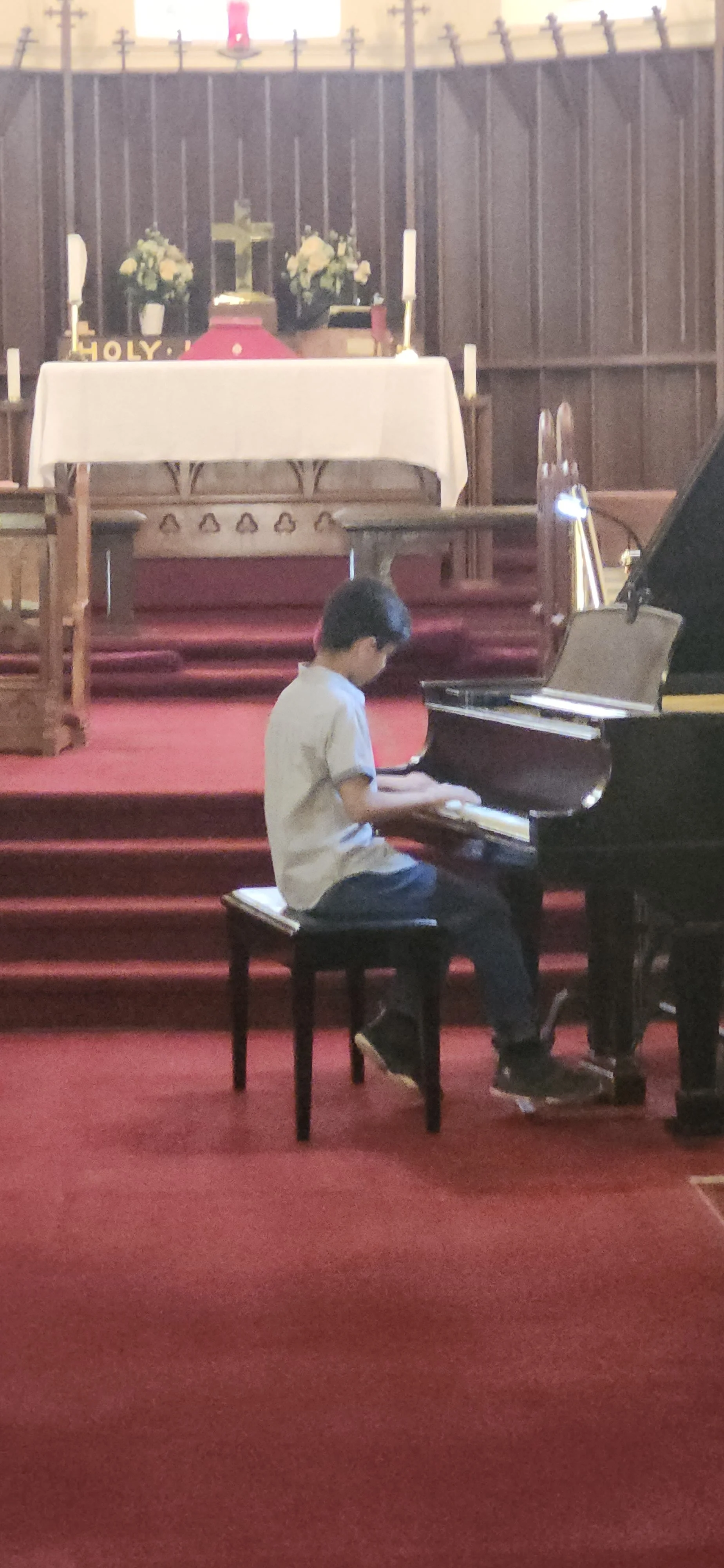 A young boy playing the piano inside a church with an altar and cross in the background.