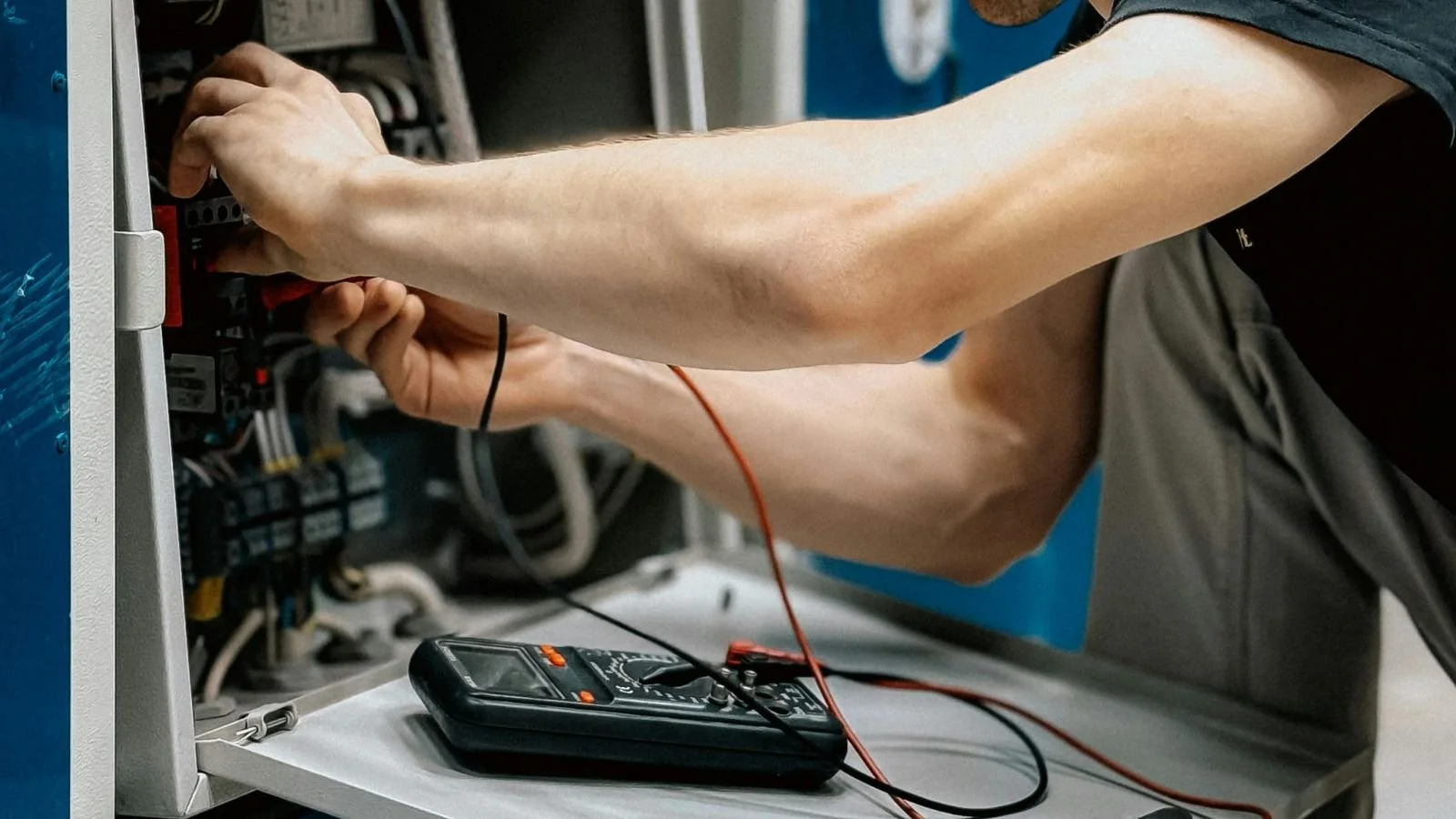 Person using a digital multimeter to test electrical components inside an electrical panel.