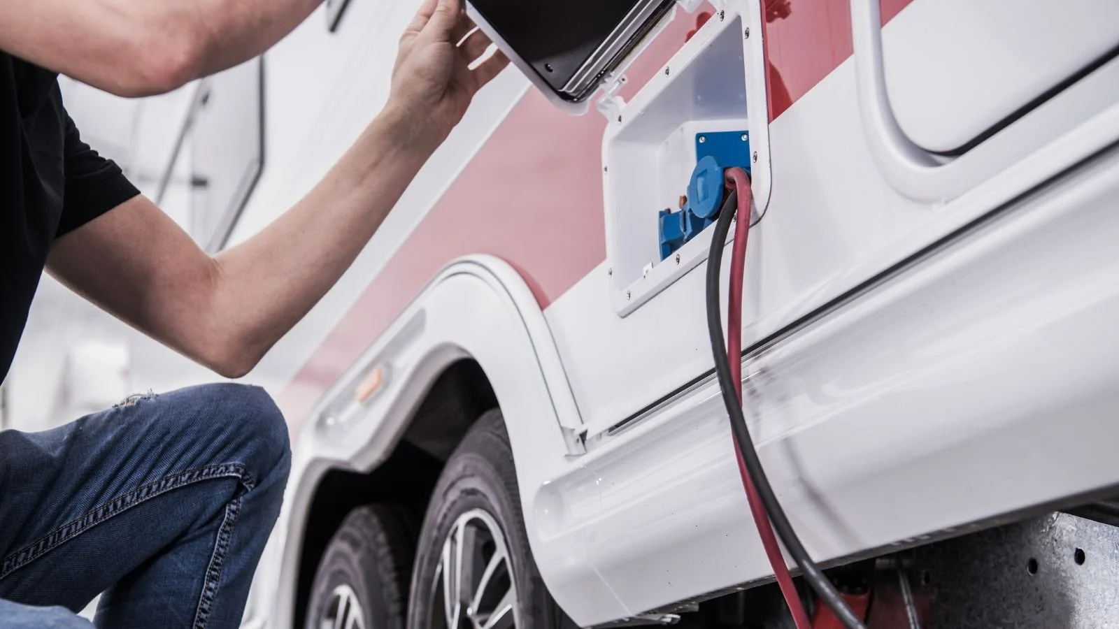 A person working on an electric vehicle charging port, connected with red and black cables.