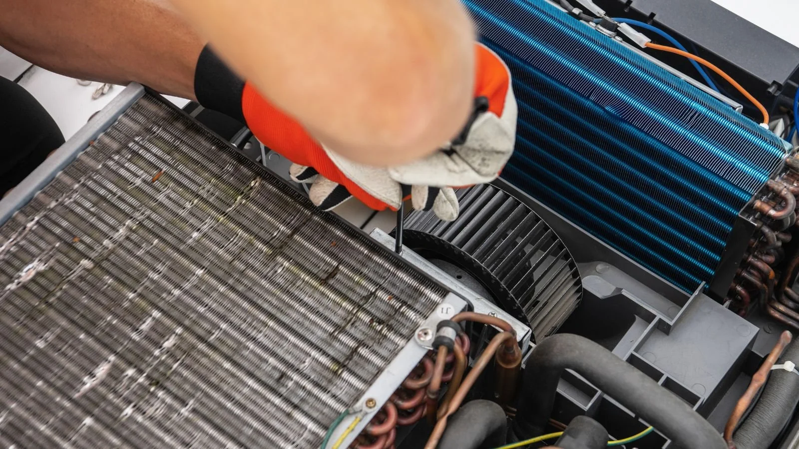 Technician's hand repairing an air conditioning unit with a screwdriver, revealing various components like coils and copper pipes.