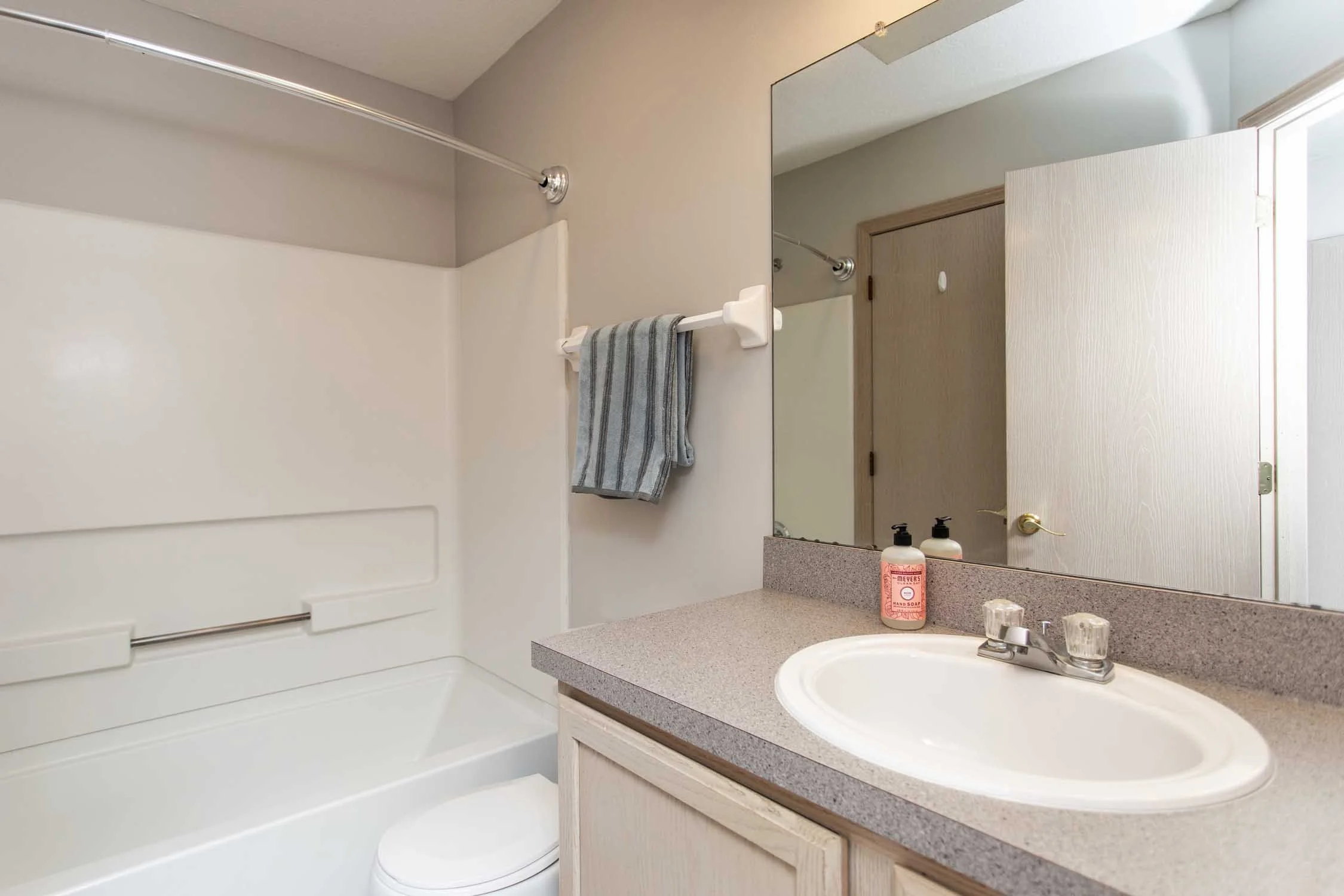 Bathroom with a sink, mirror, soap dispenser, vanity, and a bathtub with a towel hanging on a towel bar.