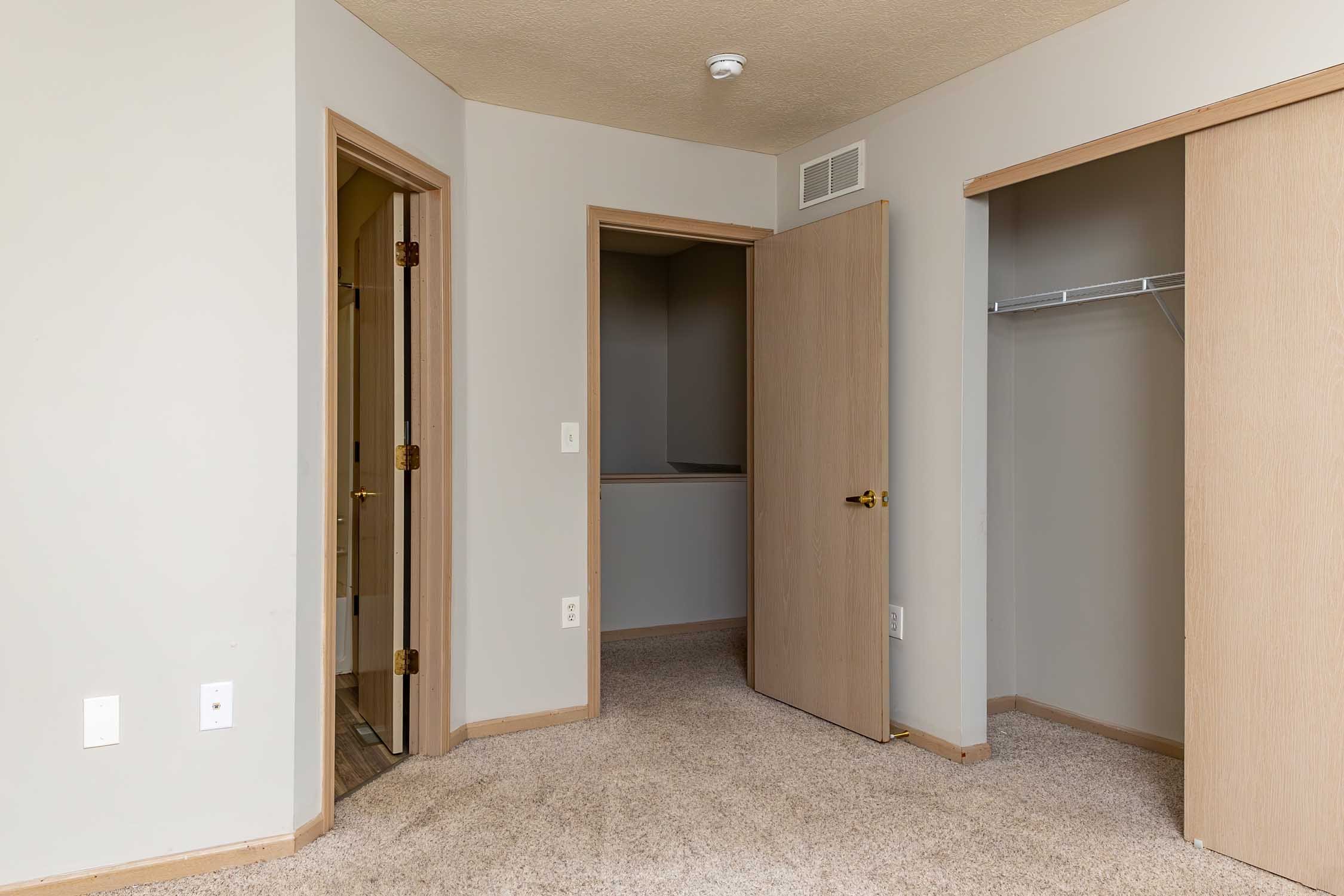 Empty room with open closet, doorway, beige carpet, and white walls.
