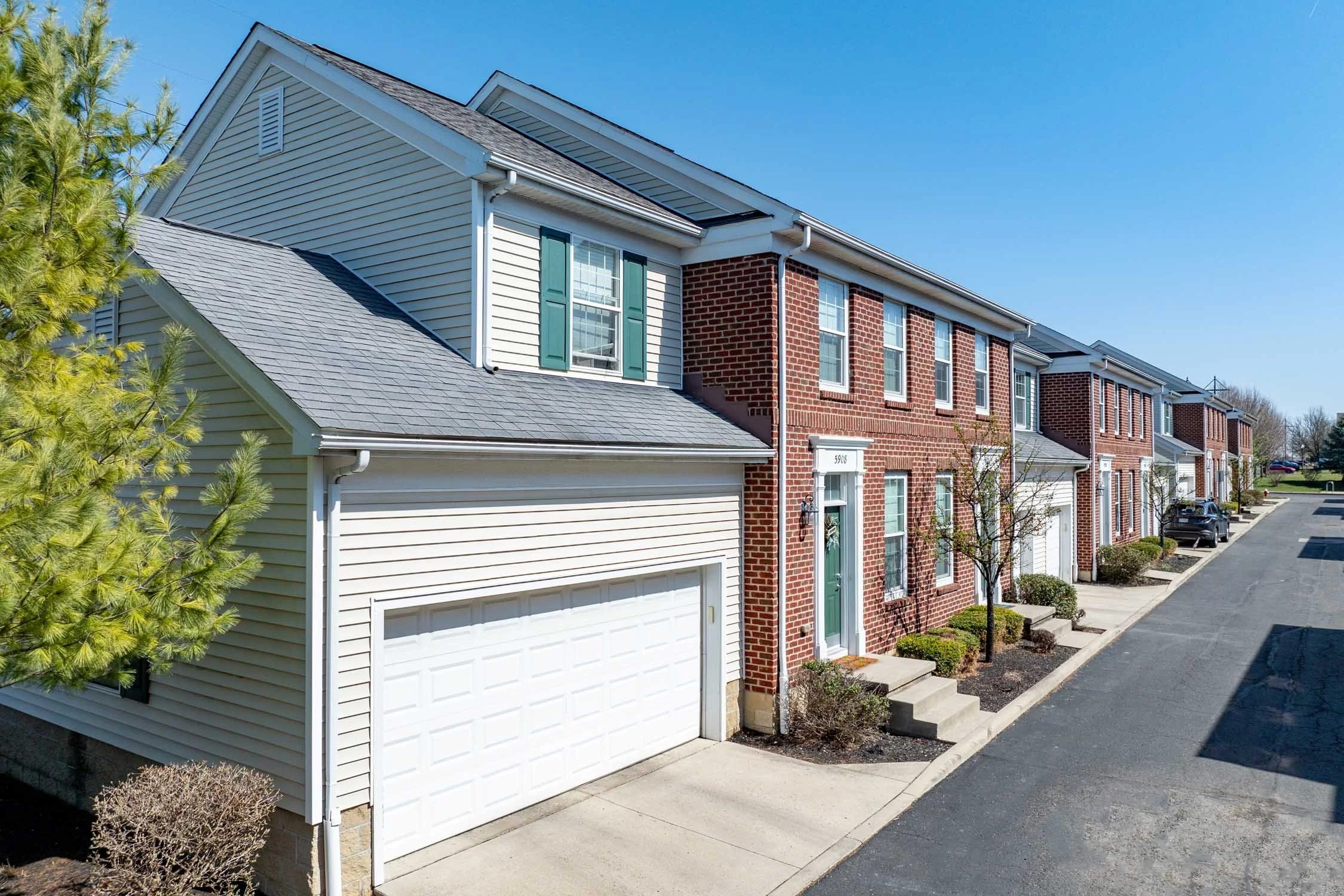 Row of modern townhouses with brick and siding exteriors, with front yards, driveways, and a clear blue sky.