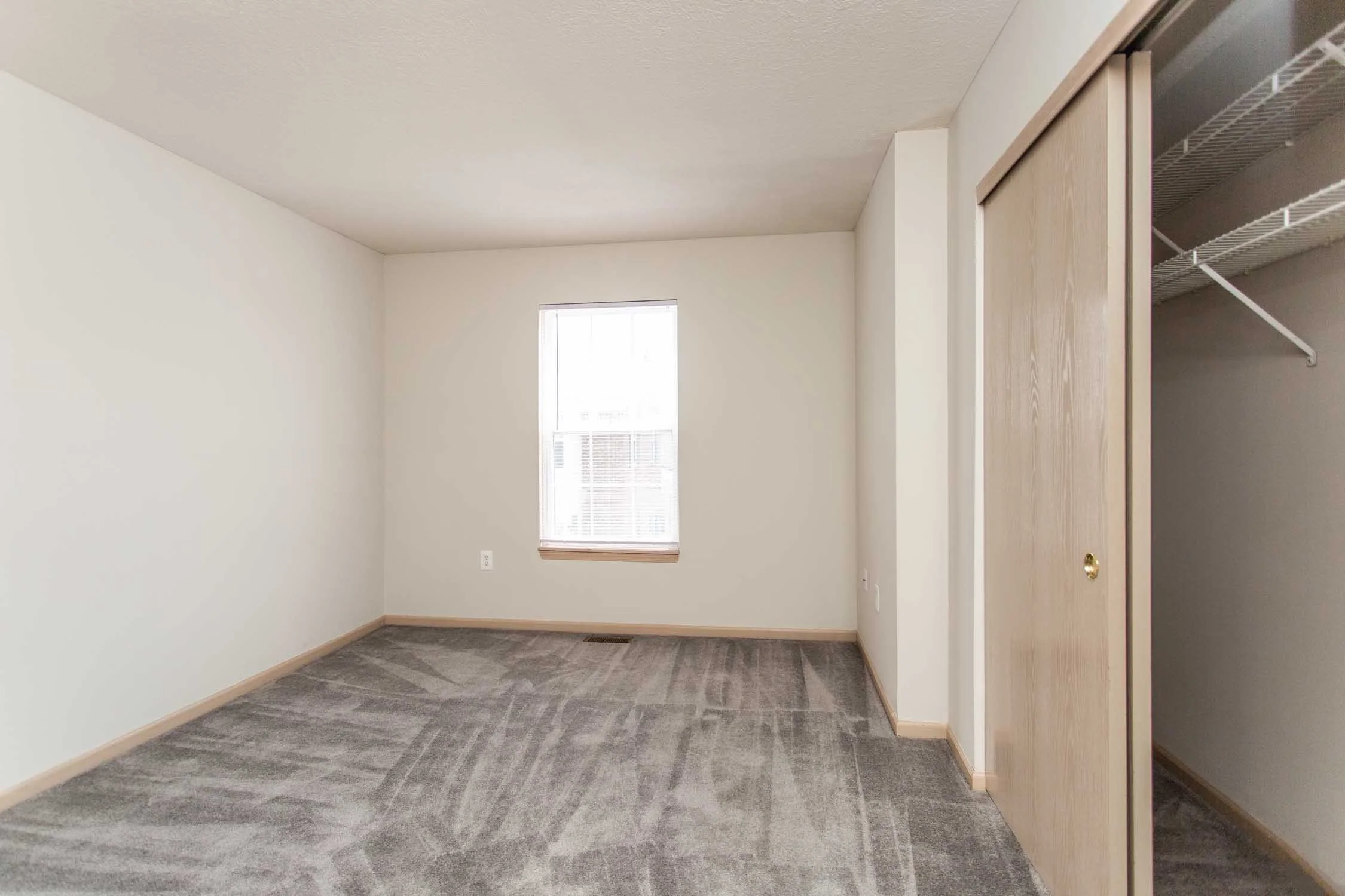 Empty room with beige walls, a small window, and a closet with sliding wooden doors and wire shelves.