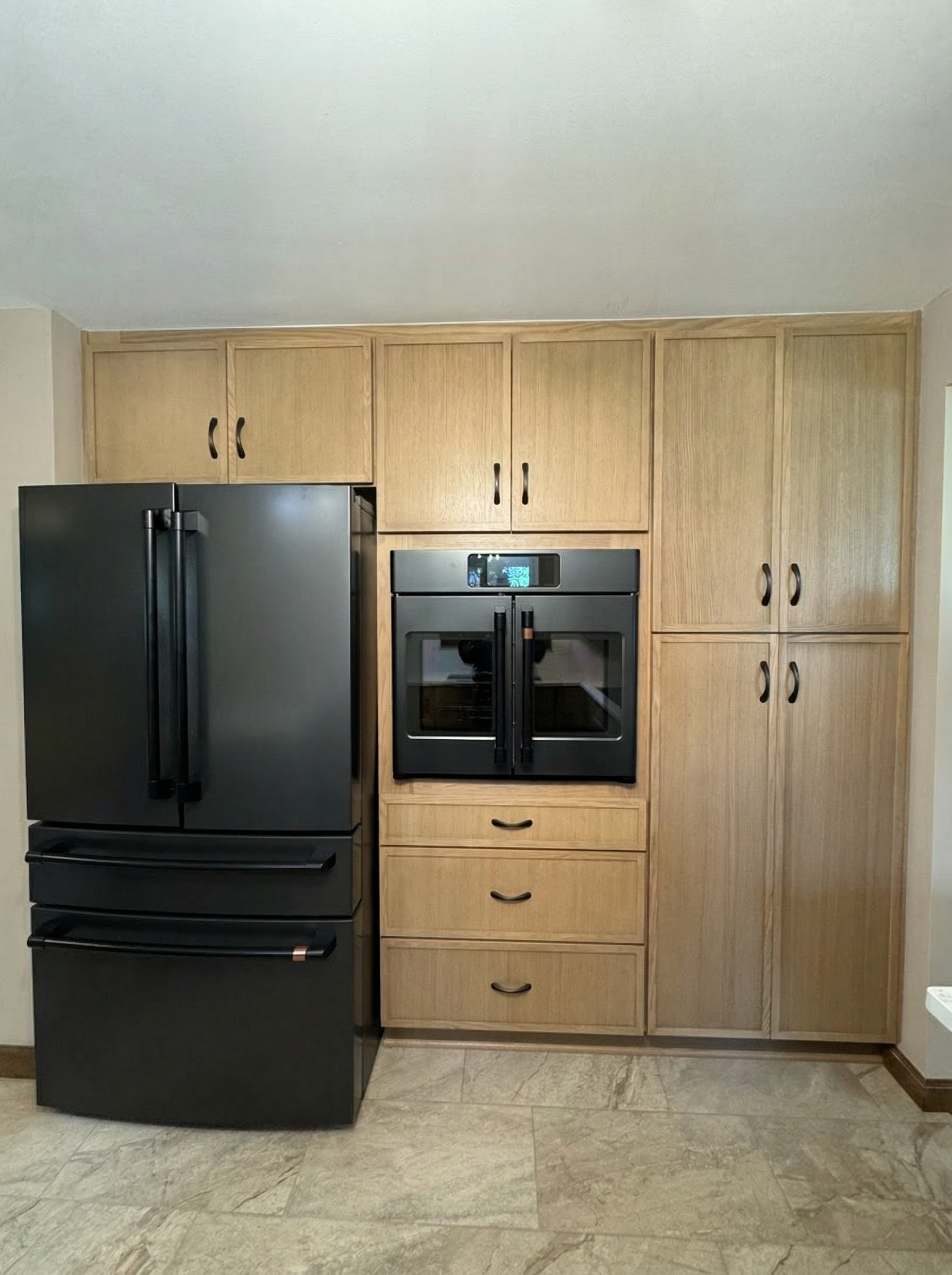 A kitchen with wooden cabinets, a black refrigerator, and a black double oven, with a tiled floor.