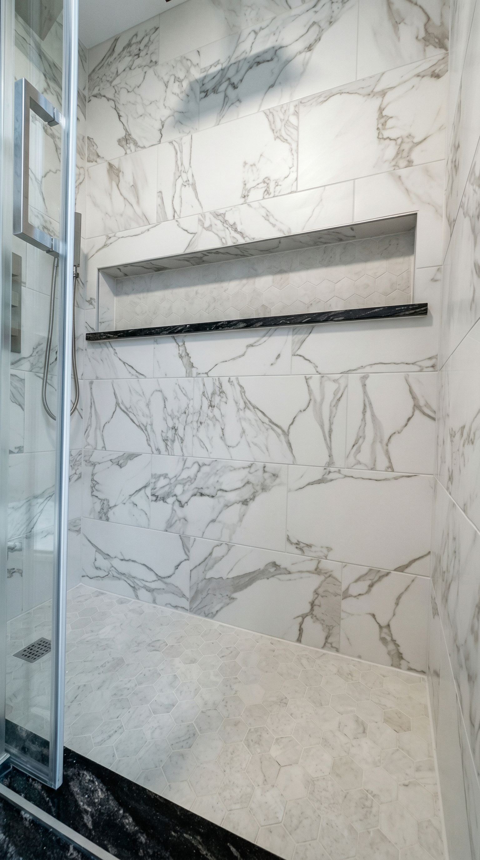 A marble tiled shower with a built-in shelf and a black marble ledge.