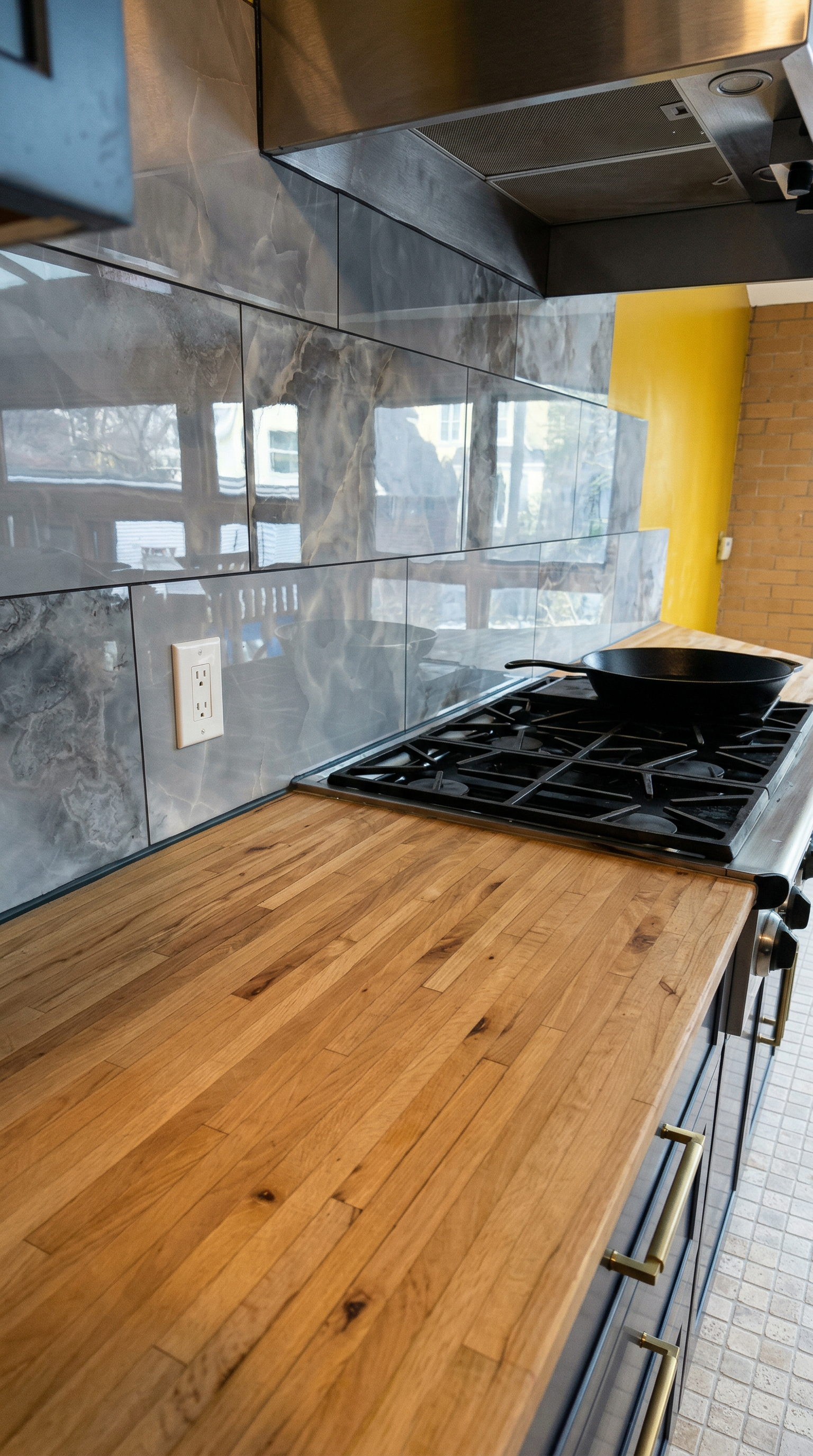 Kitchen with a wooden countertop, gray marble tile backsplash, black stove with a cast iron skillet, and a brick wall.
