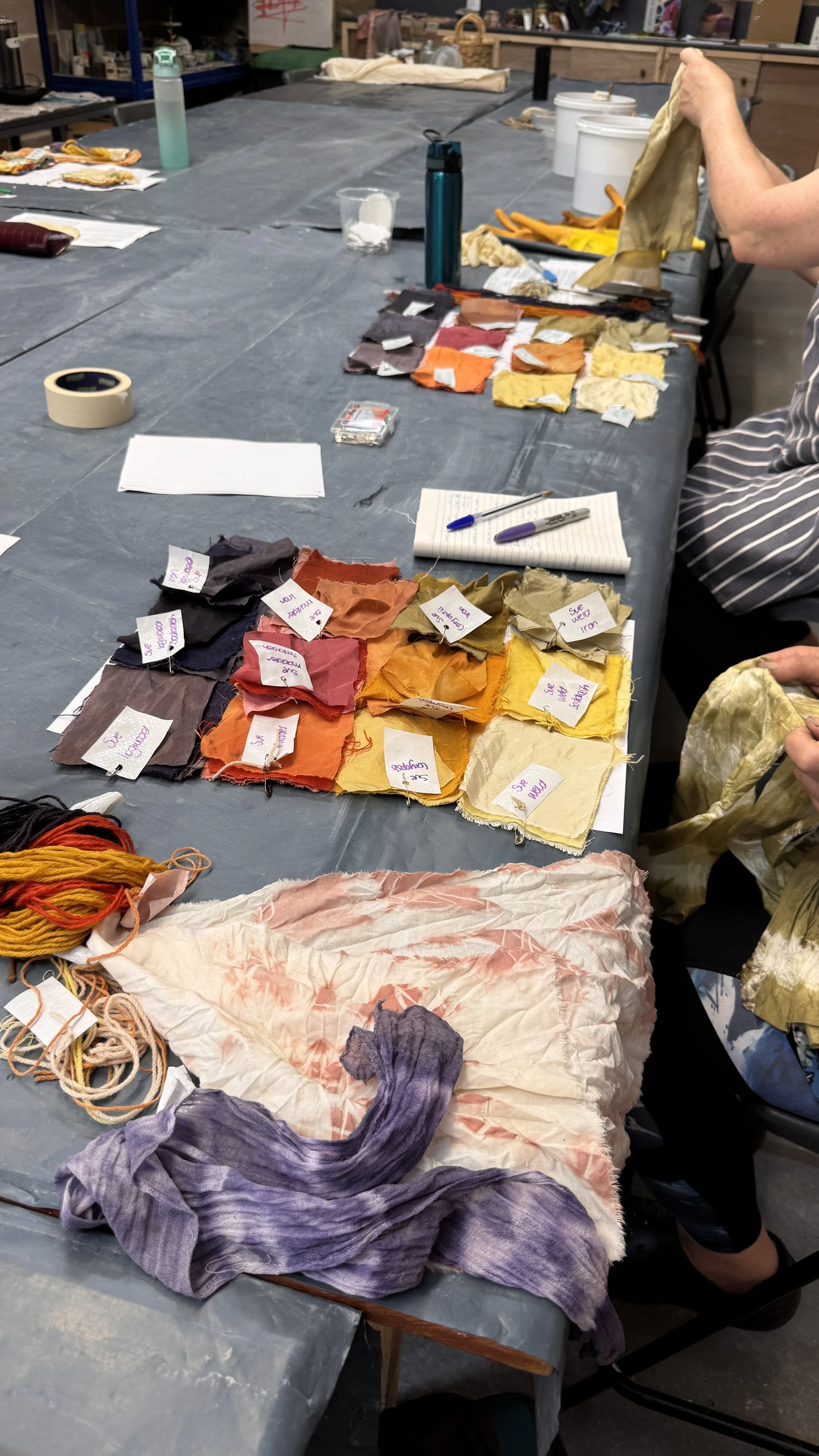 Table with fabric swatches, yarn, and notes, in a creative workspace.