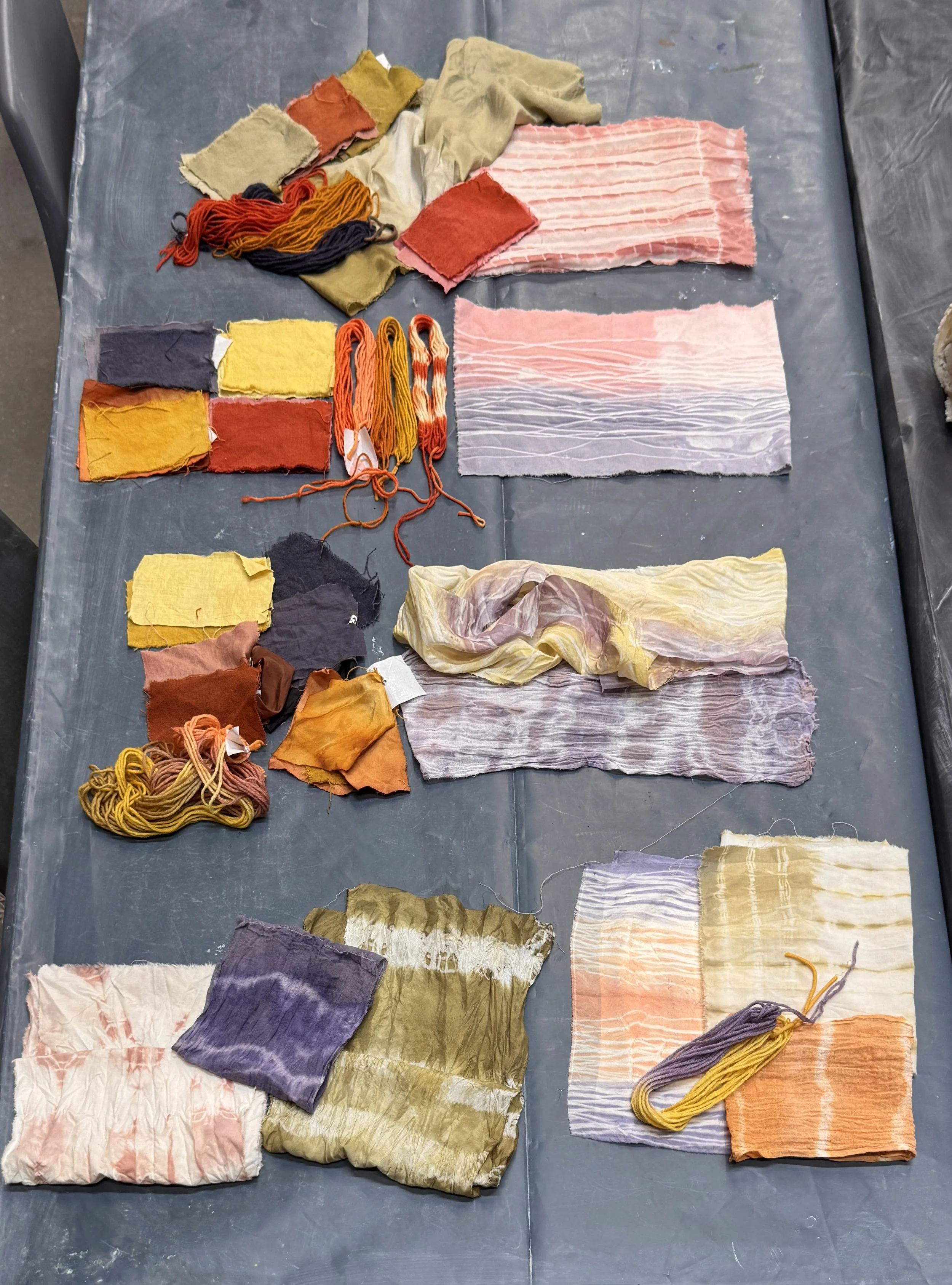 Various pieces of fabric and yarns in different colors and textures laid out on a gray surface.