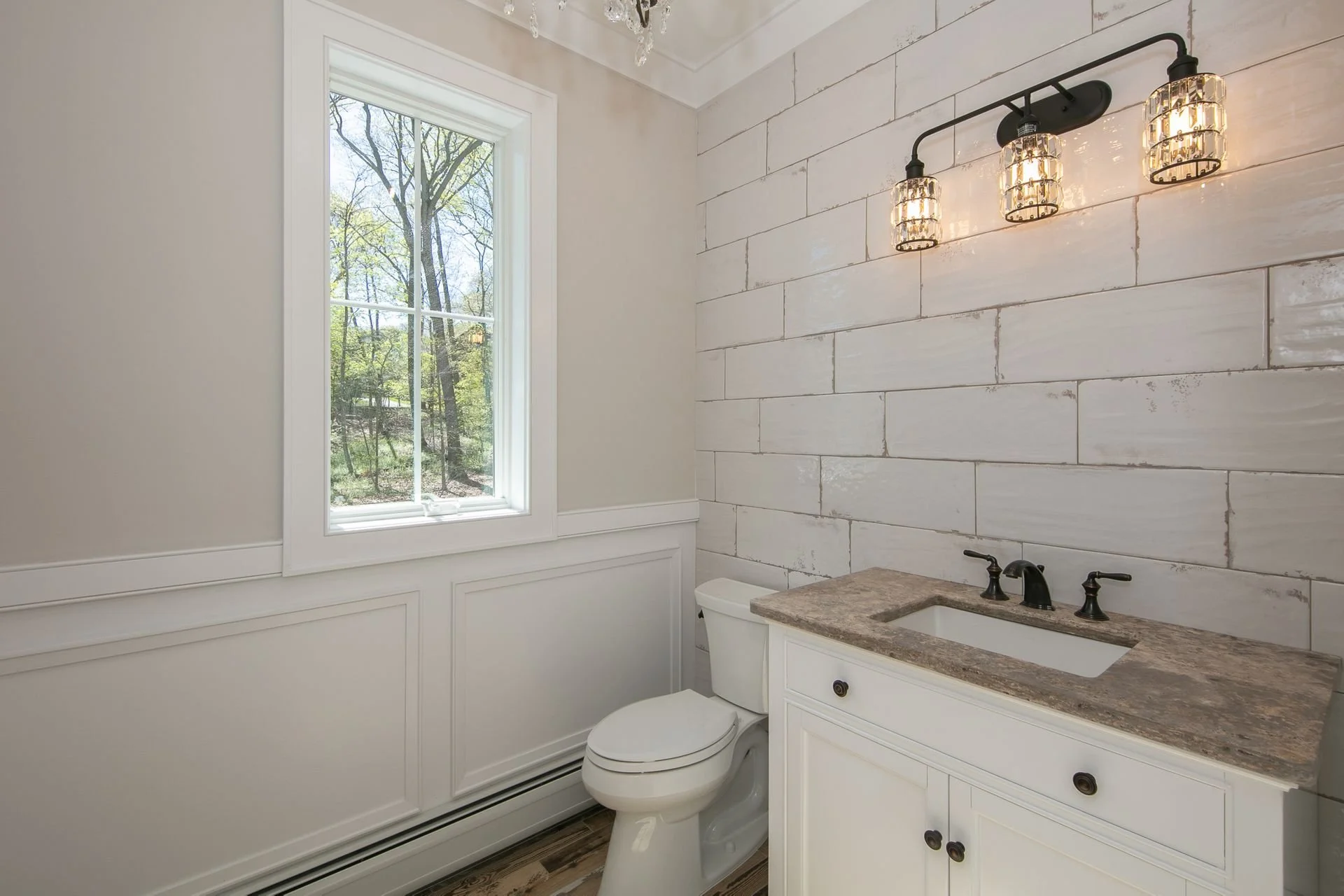 Bathroom with a window, white walls, a gray countertop with a sink, and a light fixture with three glass shades.