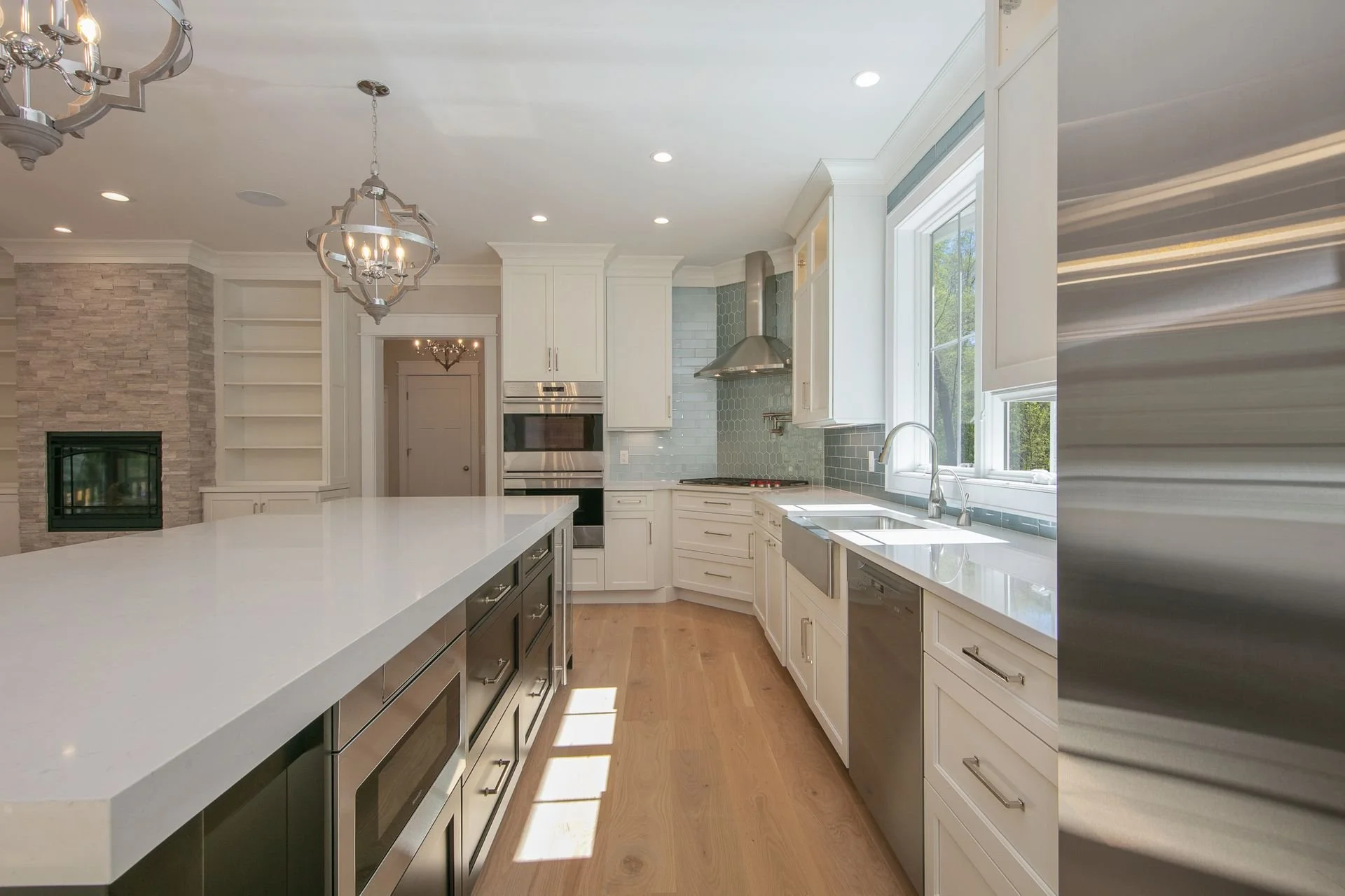 Modern kitchen with white cabinets, a large white island, stainless steel appliances, and a window overlooking trees.