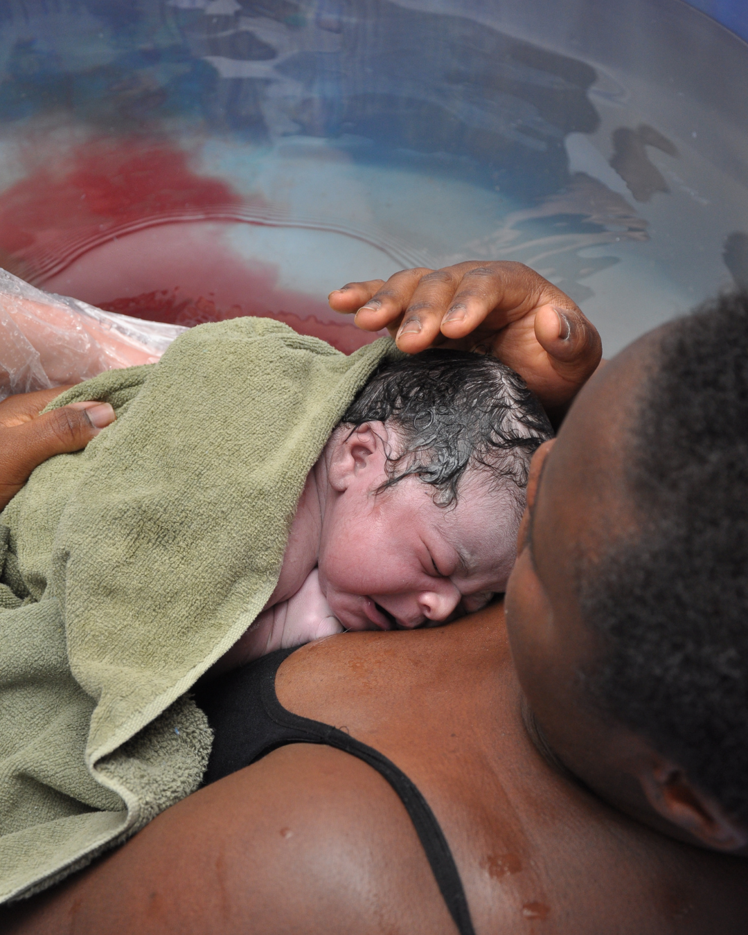 A newborn baby being born in a water birth, with a woman holding the baby and supporting it in the water