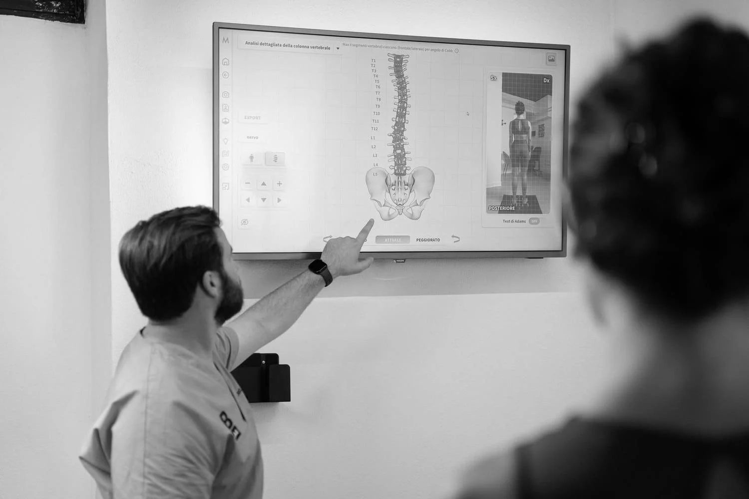 Medical professional explaining a diagram of the human spine on a digital screen to a patient.