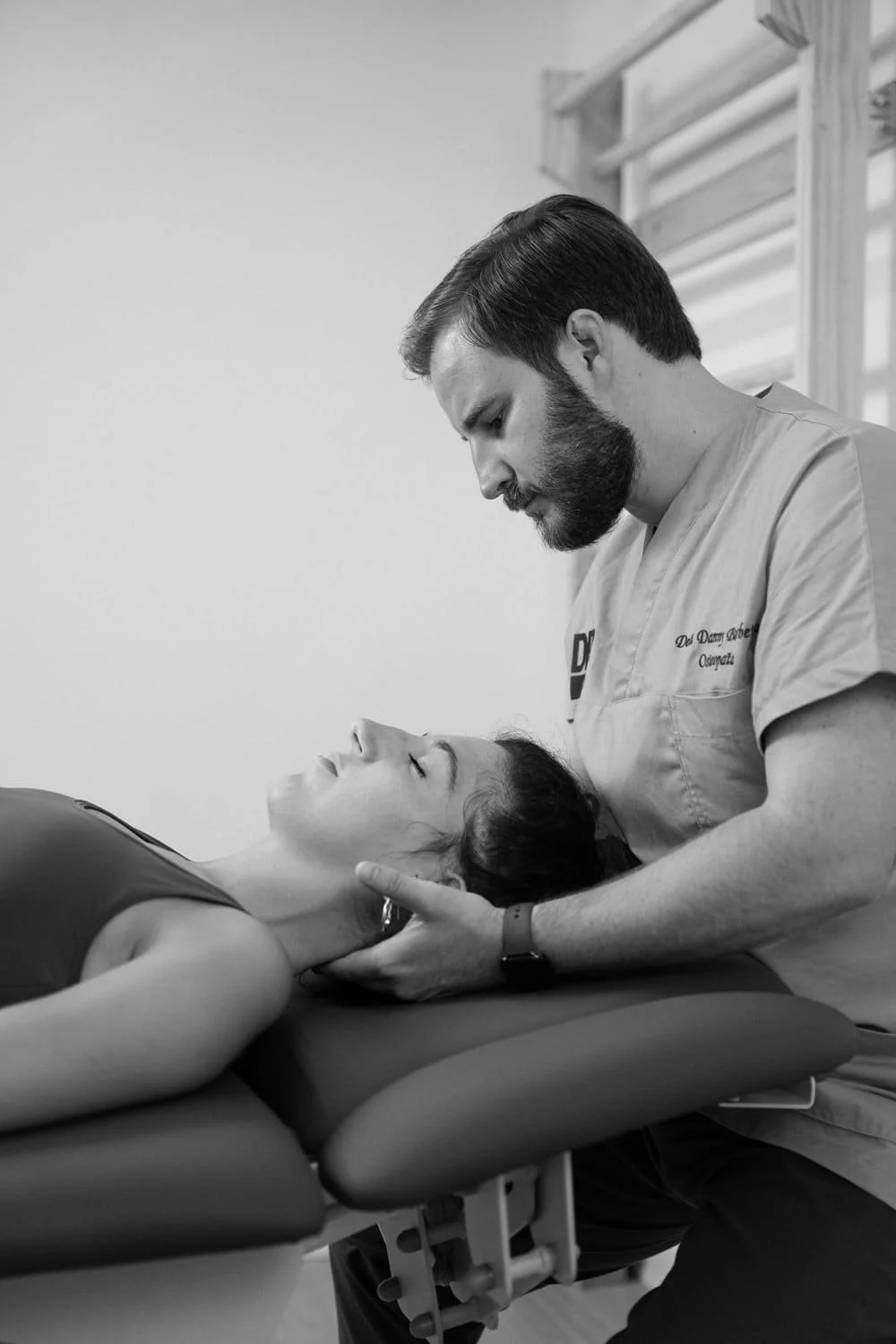 A male chiropractor adjusting a female patient's neck on a treatment table in a clinic setting.