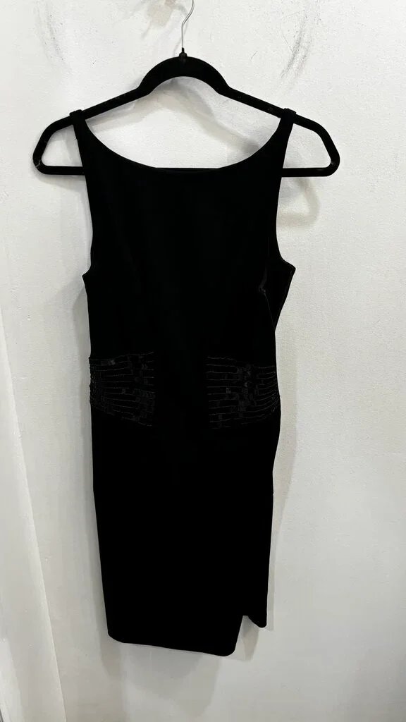 Black sleeveless dress hanging on a black hanger against a white wall.