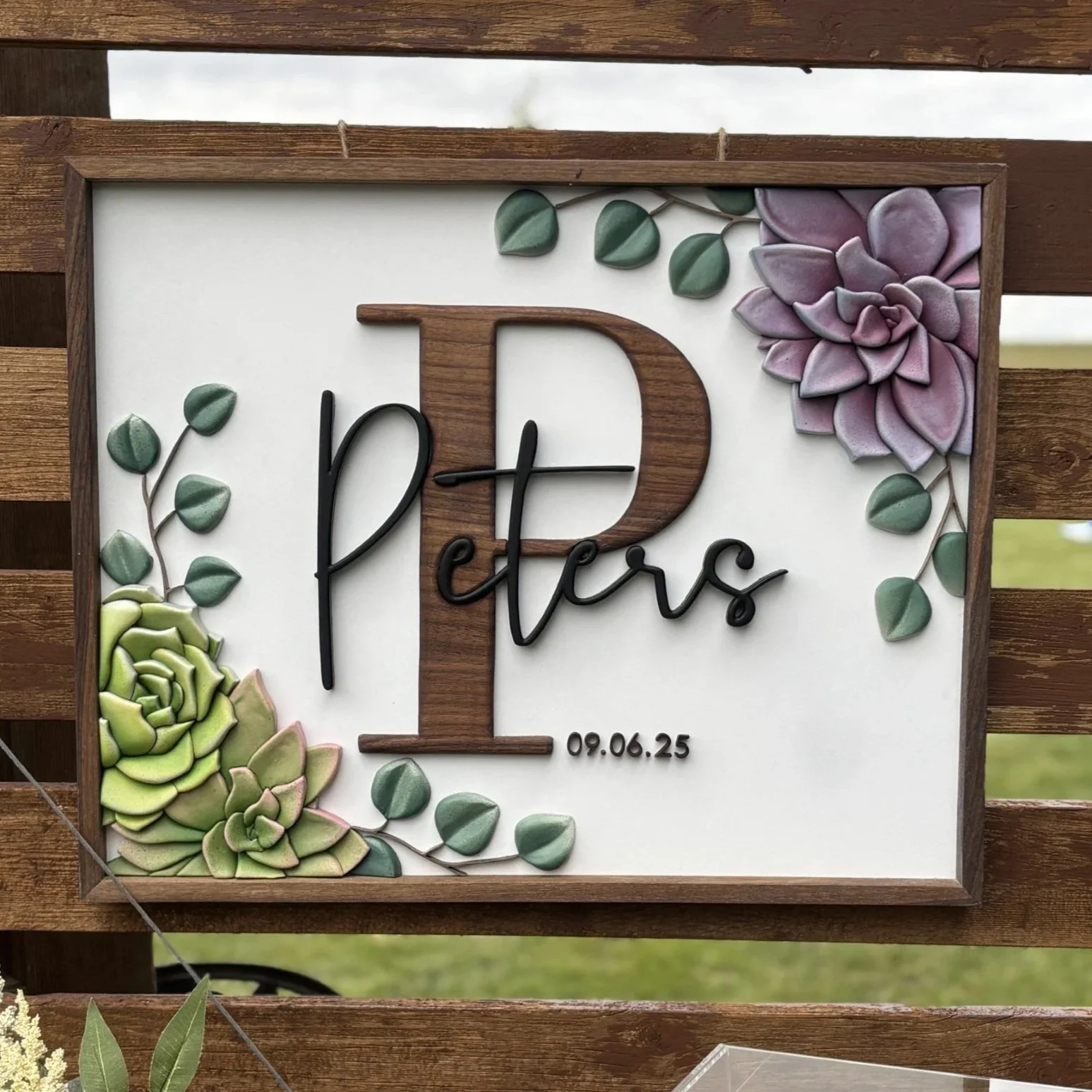 Decorative sign with the letter 'T' made of wood, surrounded by colorful succulent plants, with the words 'lovers' and the date '09.06.25' written on it.