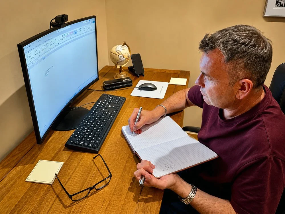 Andy from Cherry Tree Business Consulting sitting at a desk, writing in a notebook while looking at a large computer monitor.
