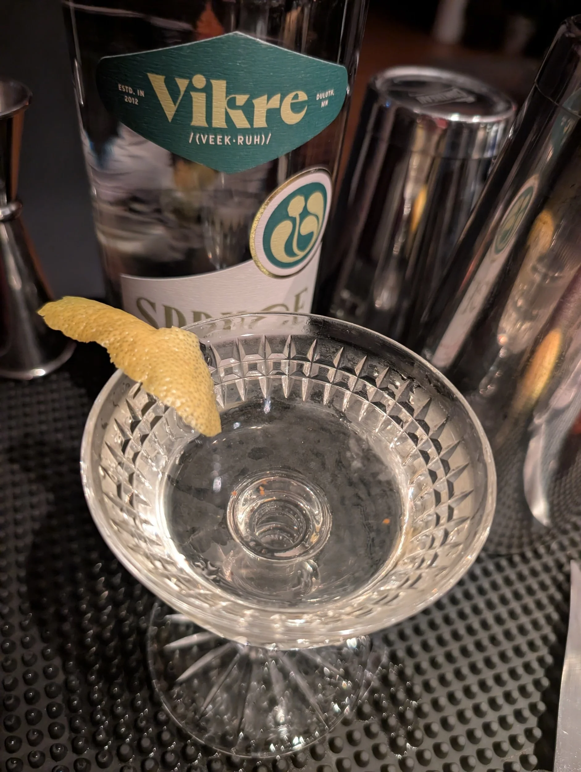 image of martini with lemon peel garnish, in a vintage glass, with a bottle of Vikre Spruce Boreal gin and some shakers behind it.