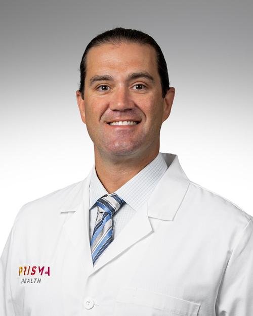 Male doctor wearing a white lab coat with a blue striped tie, smiling, against a gray background.