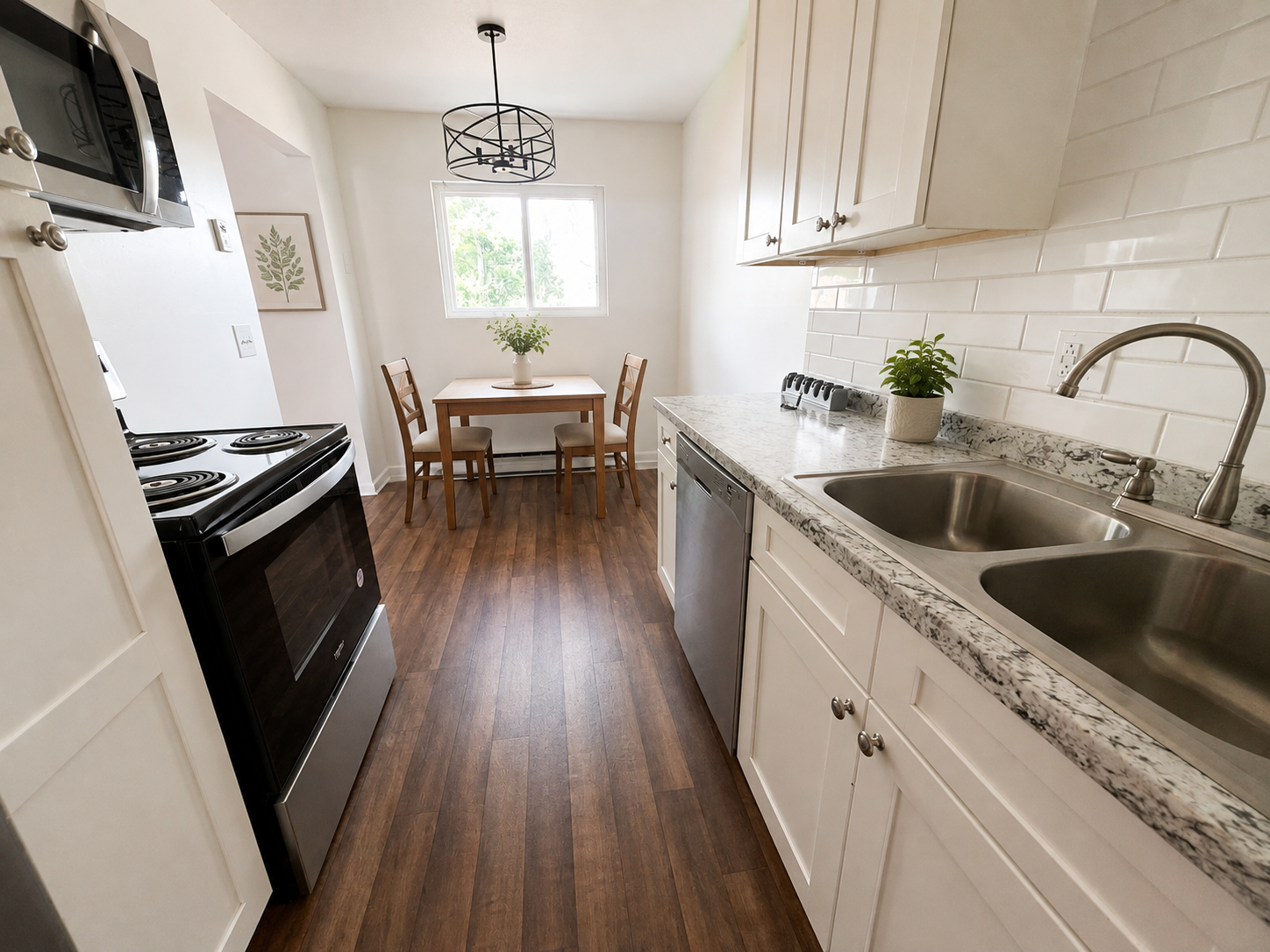 Kitchen with white cabinets, granite countertops, stainless steel sink, black electric stove, microwave, small dining table with two chairs, and hardwood flooring.