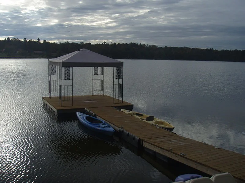 A lakeside dock with a gazebo and kayaks under an overcast sky.