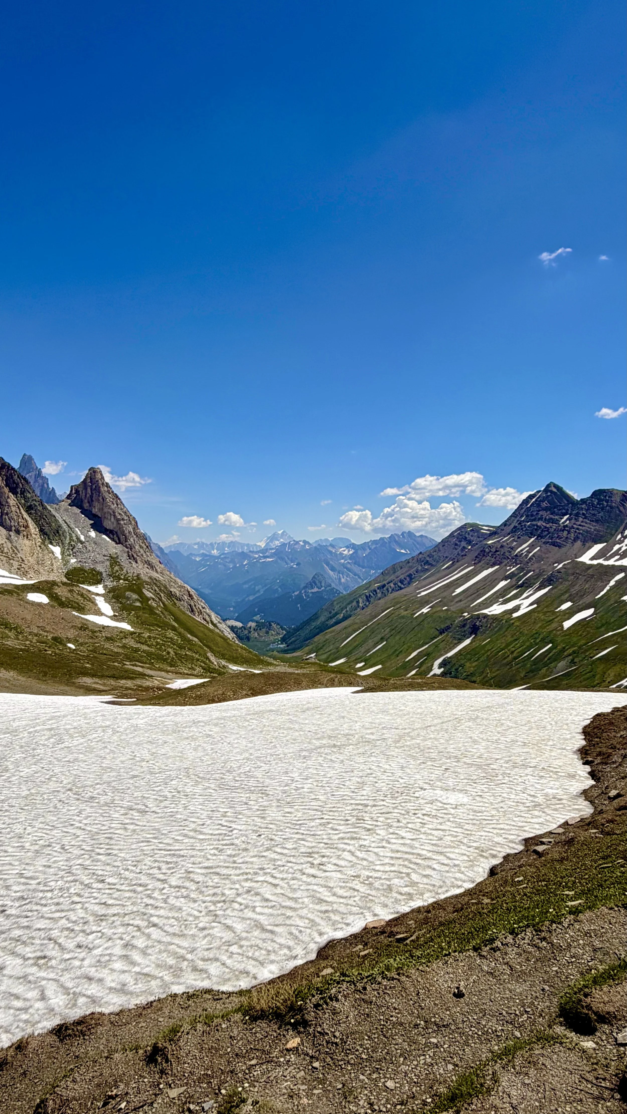 Snow-covered mountain valley with rugged mountain peaks in the background and a clear blue sky.