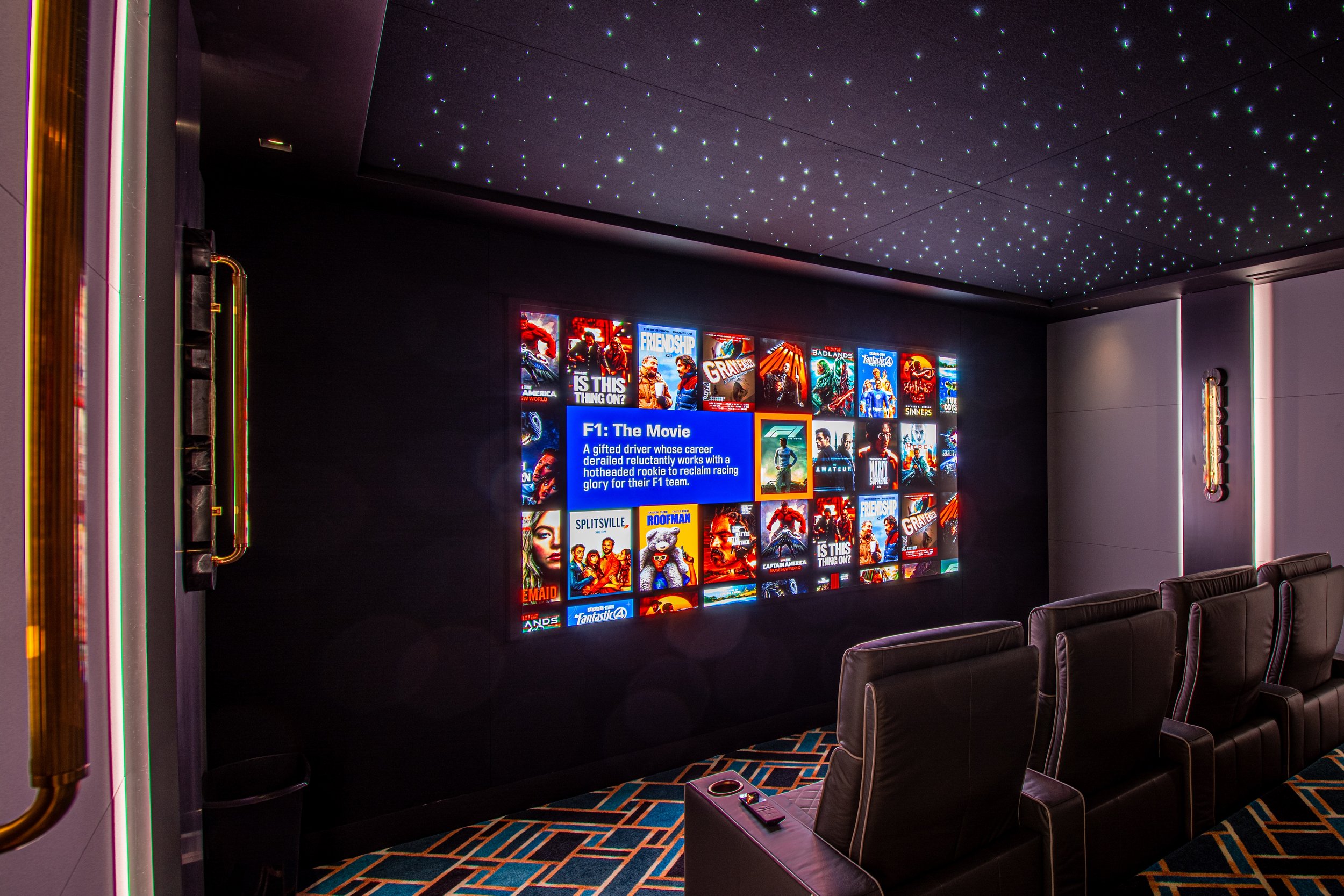A movie theater lobby with a large wall display showcasing various movie posters, a digital screen providing film information, and seating chairs. The ceiling has a starry sky effect with small glowing lights.