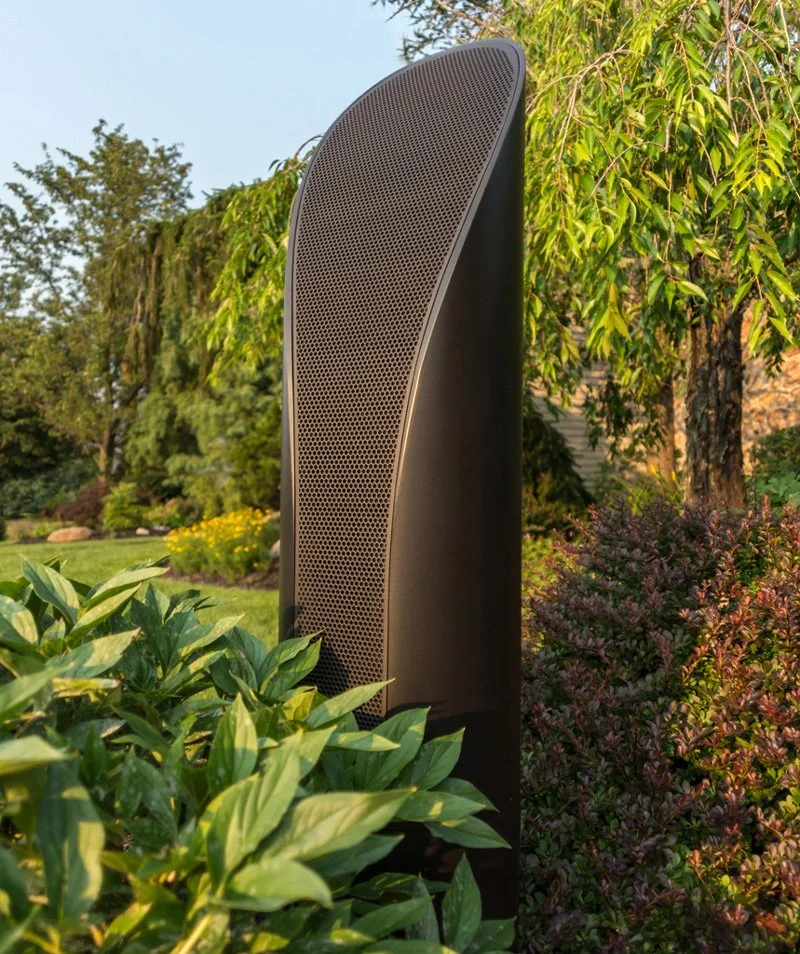 Large outdoor black speaker surrounded by green bushes and trees in a garden