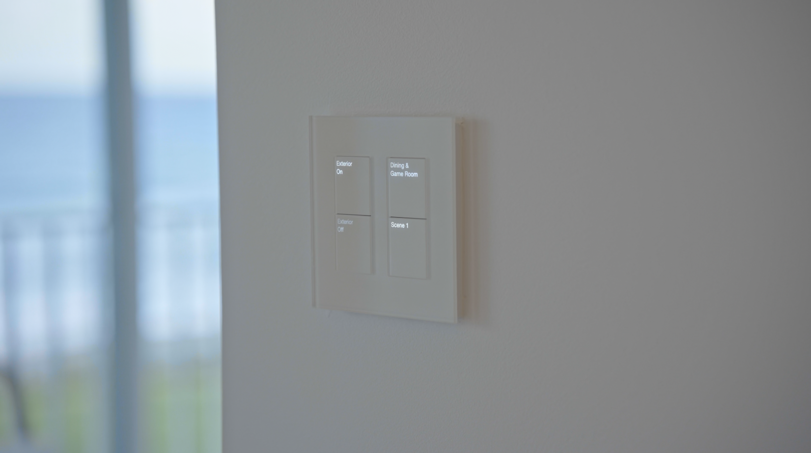 Four-button lighting keypad on a wall with the ocean visible beyond