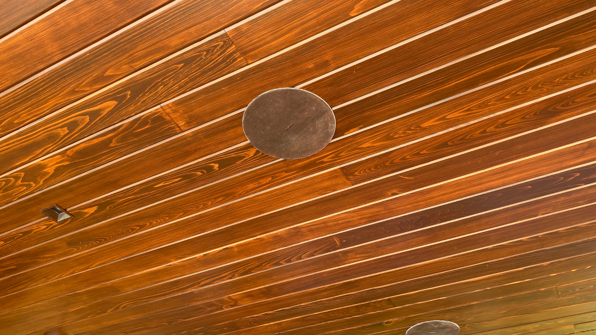 Speaker set flush into the stained wood sauna ceiling, finished so the ceiling stays the subject