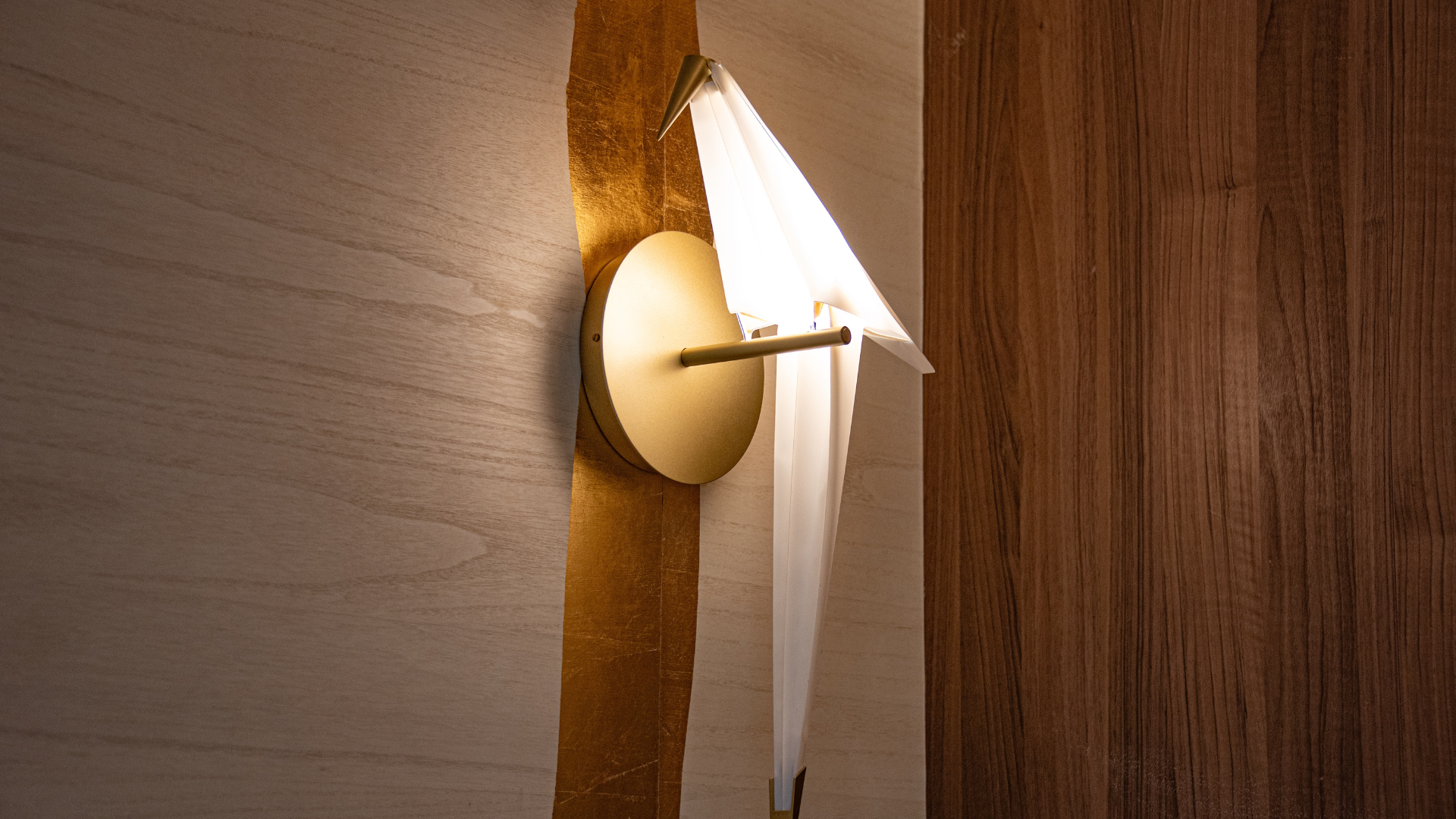 A modern wall-mounted light fixture with a circular base and a white triangular shade, mounted on a wall with beige and wood paneling.
