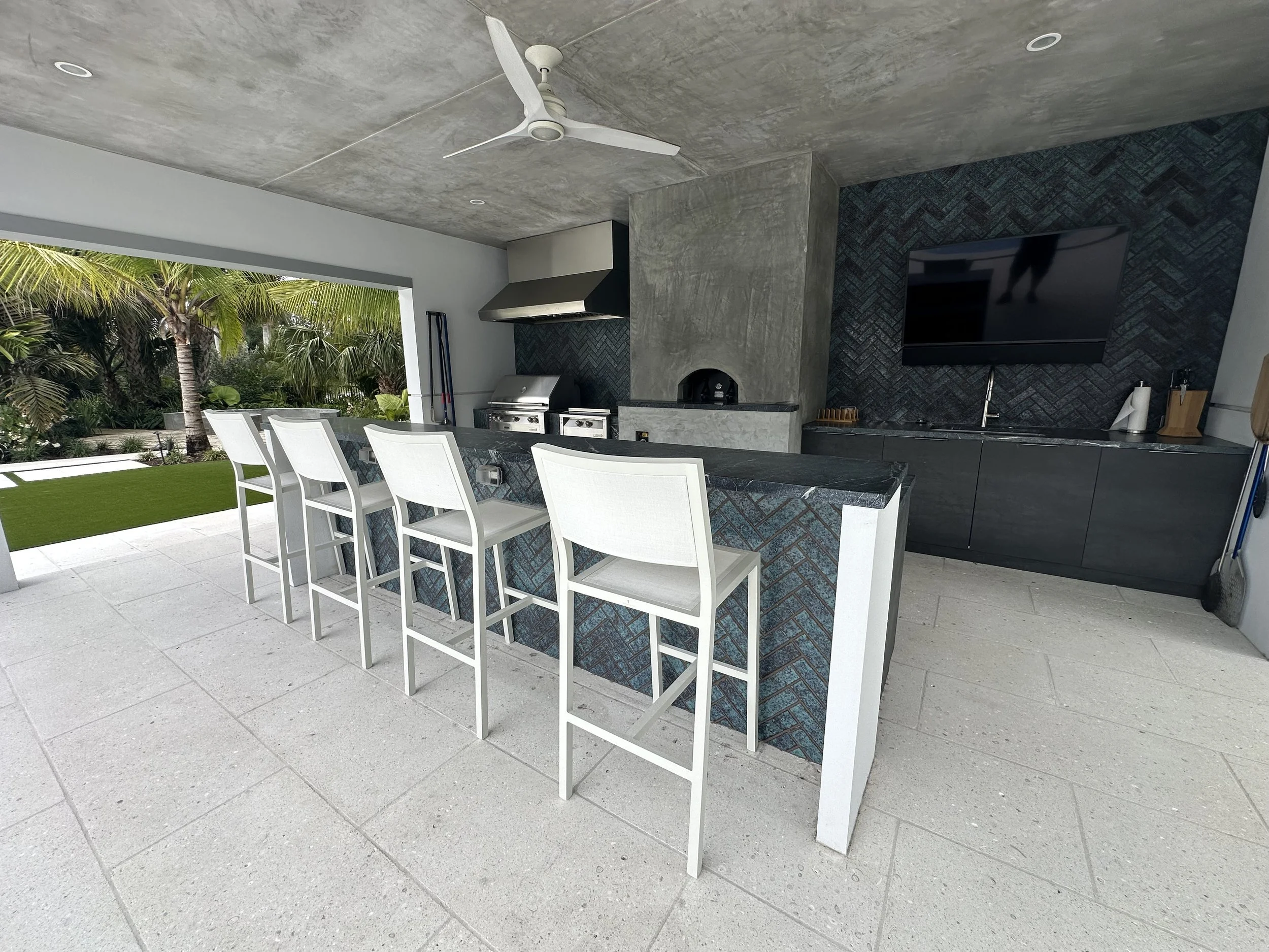 Pool house and outdoor kitchen across the pool deck, with audio at the bar