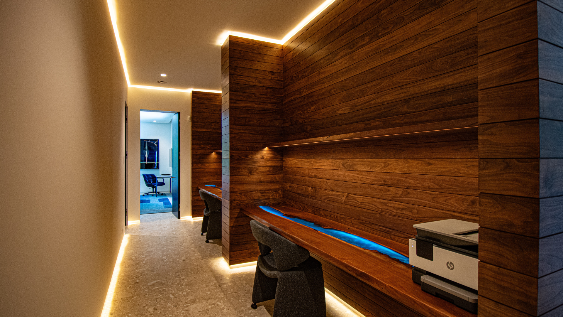 Linear lighting running the length of a walnut office corridor with a live-edge desk